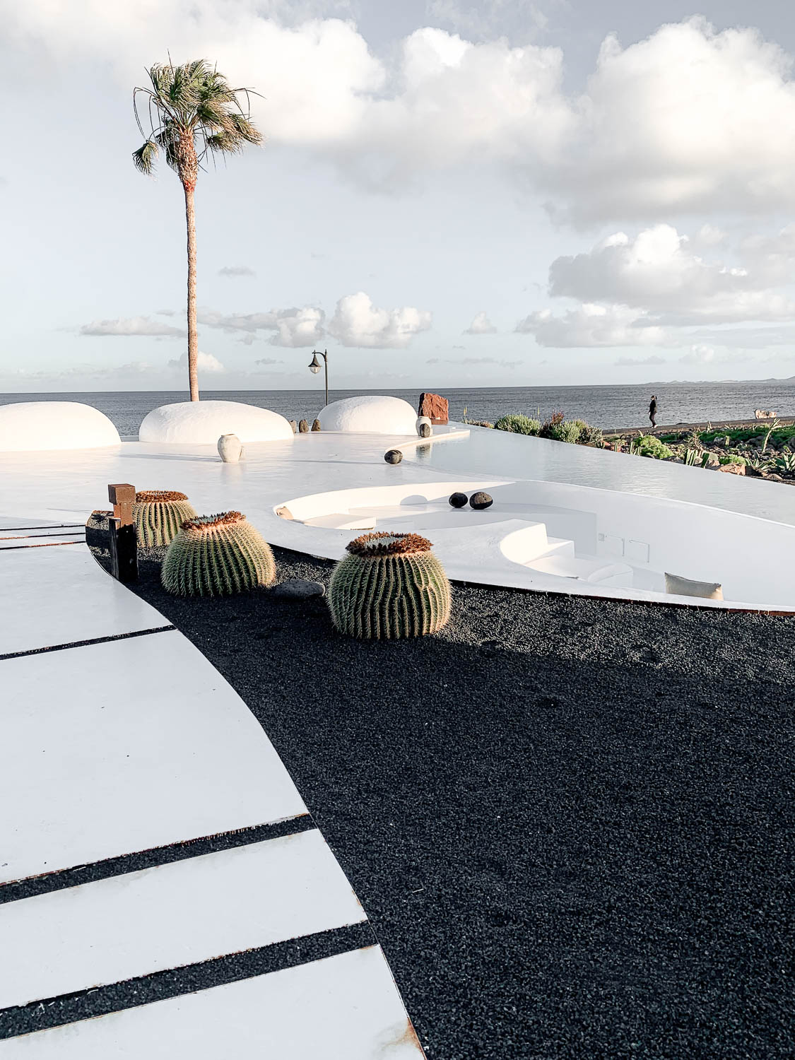Bílá terasa s barelkovými kaktusy a černým pikonem u moře – barevná paleta bílá, černá a zelená na Lanzarote