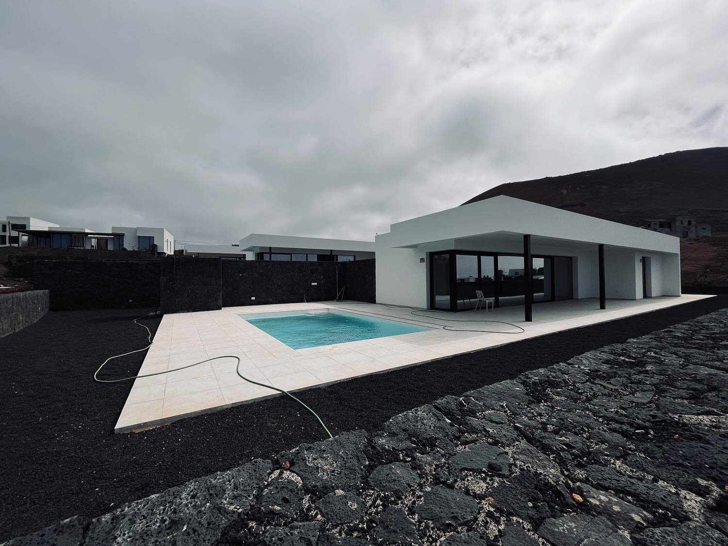 Novostavba minimalistické bílé vily s bazénem na černé lávové půdě, dramatická oblačná obloha, Lanzarote