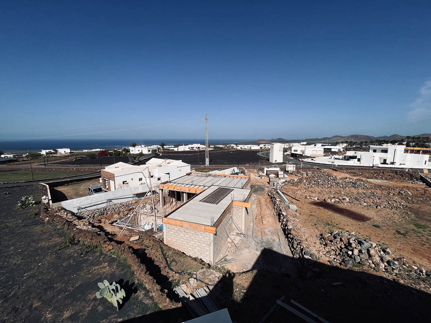 Letecký pohled na rozestavěné domy ve čtvrti Las Breñas s výhledem na oceán a hory Lanzarote, opuncie v popředí