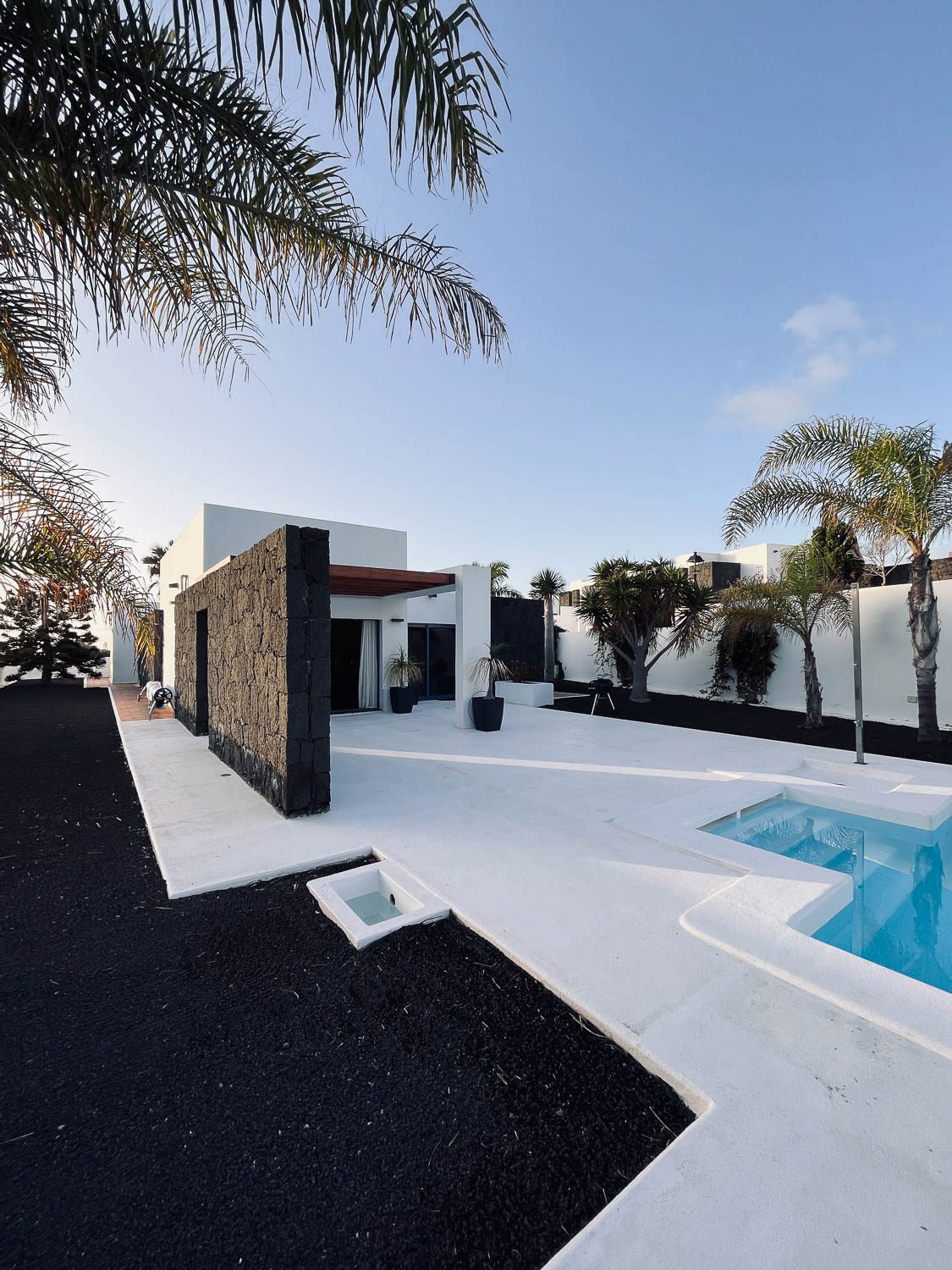 Exteriér moderní černo-bílé vily s lávovou kamennou dekorativní stěnou a prostorem u bazénu, Playa Blanca