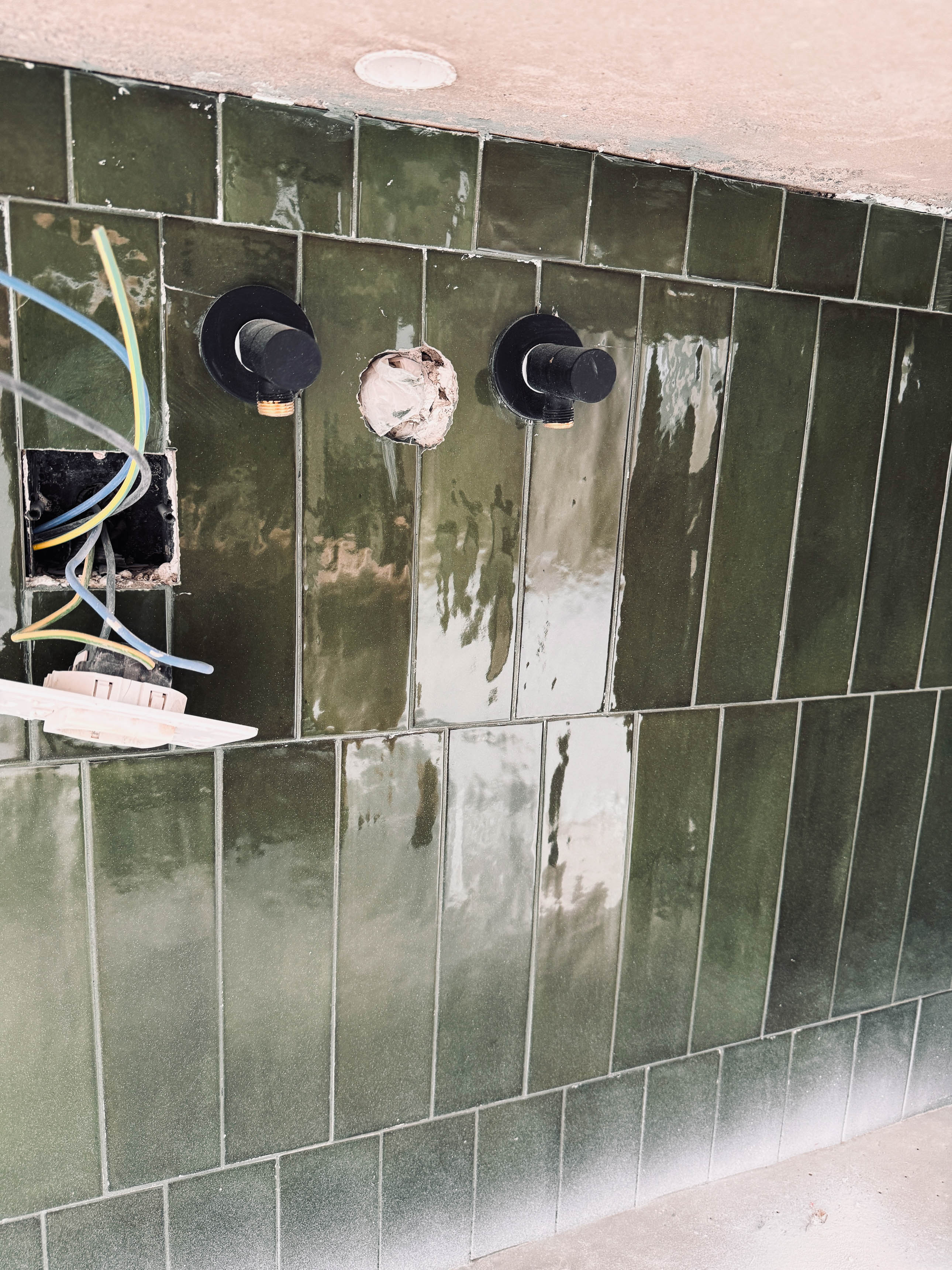 Detail zelených keramických obkladů s namontovanými černými bateriemi a odkrytou elektroinstalací v krabici