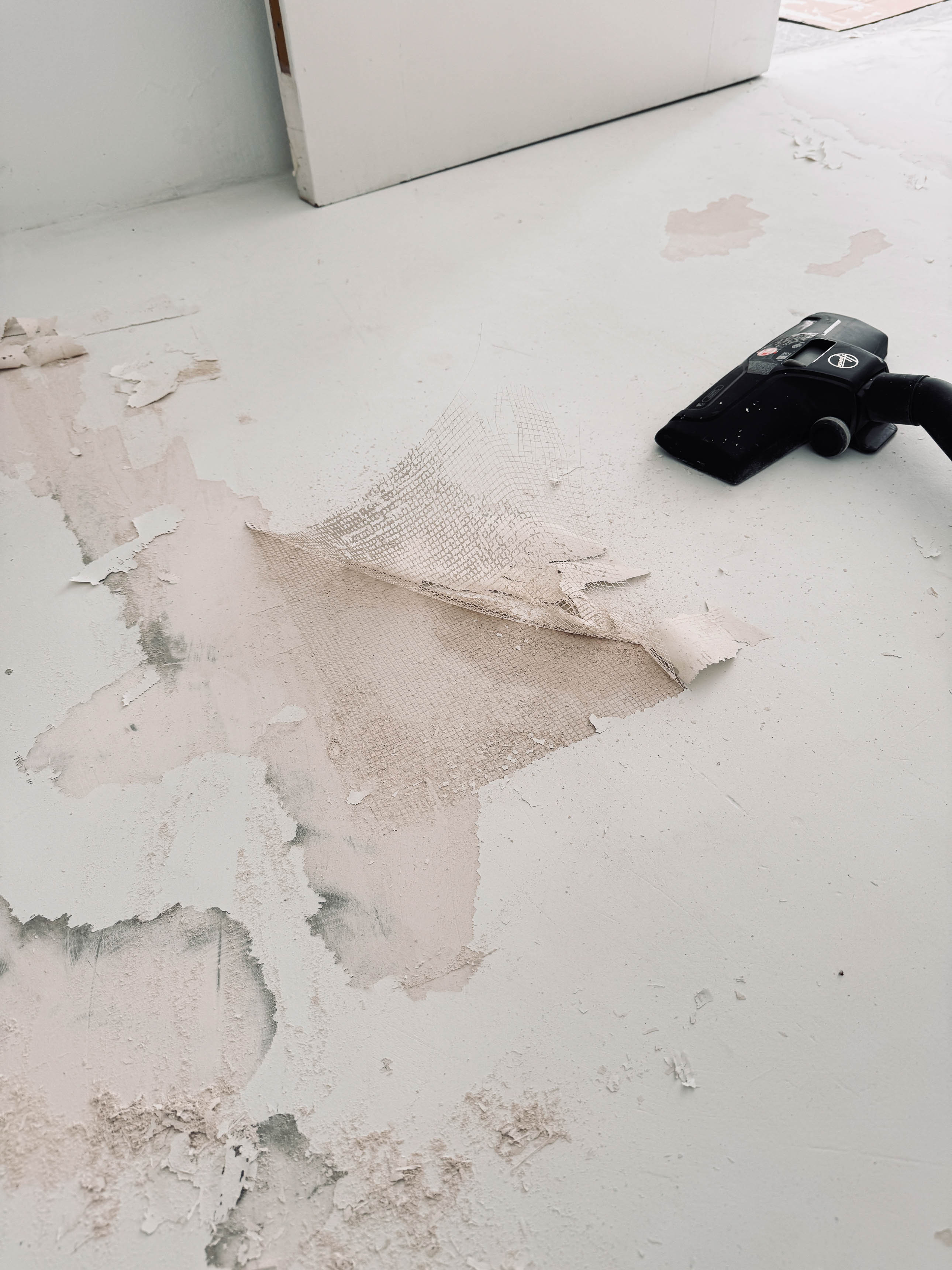 Podlaha s rozsáhlým odlupováním nátěru, záplatou ze skleněné síťoviny a vysavačem vedle