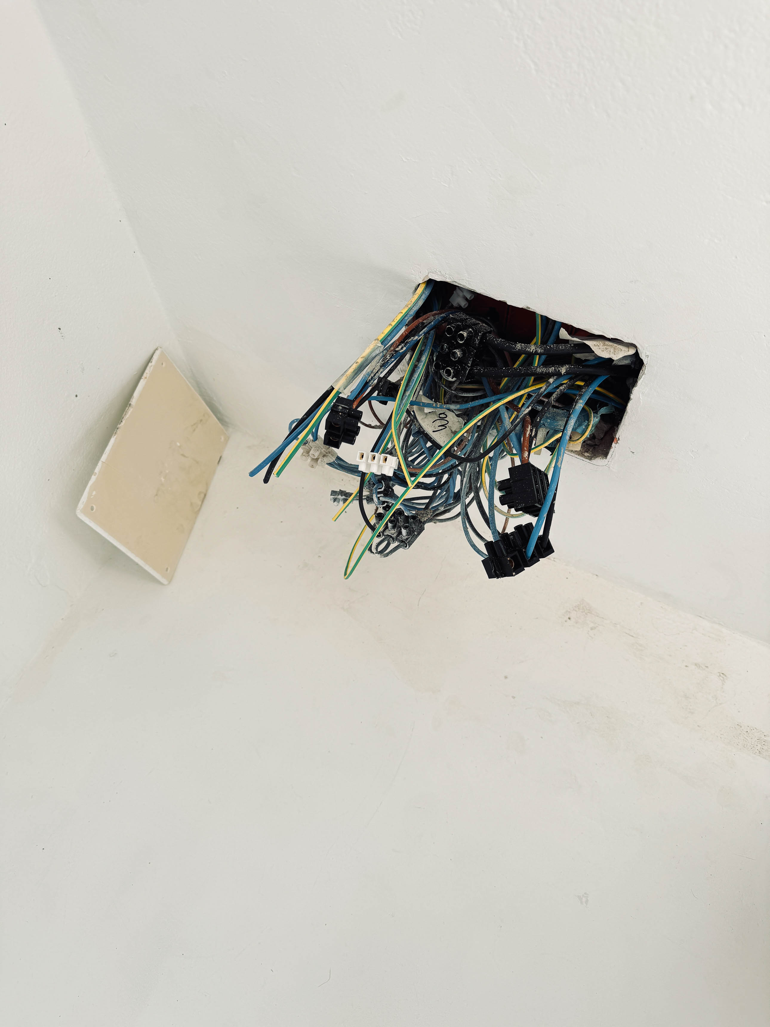 Chaos zapletených barevných elektrických kabelů visících skrz díru ve stropě – ukázka nekvalitní elektroinstalace