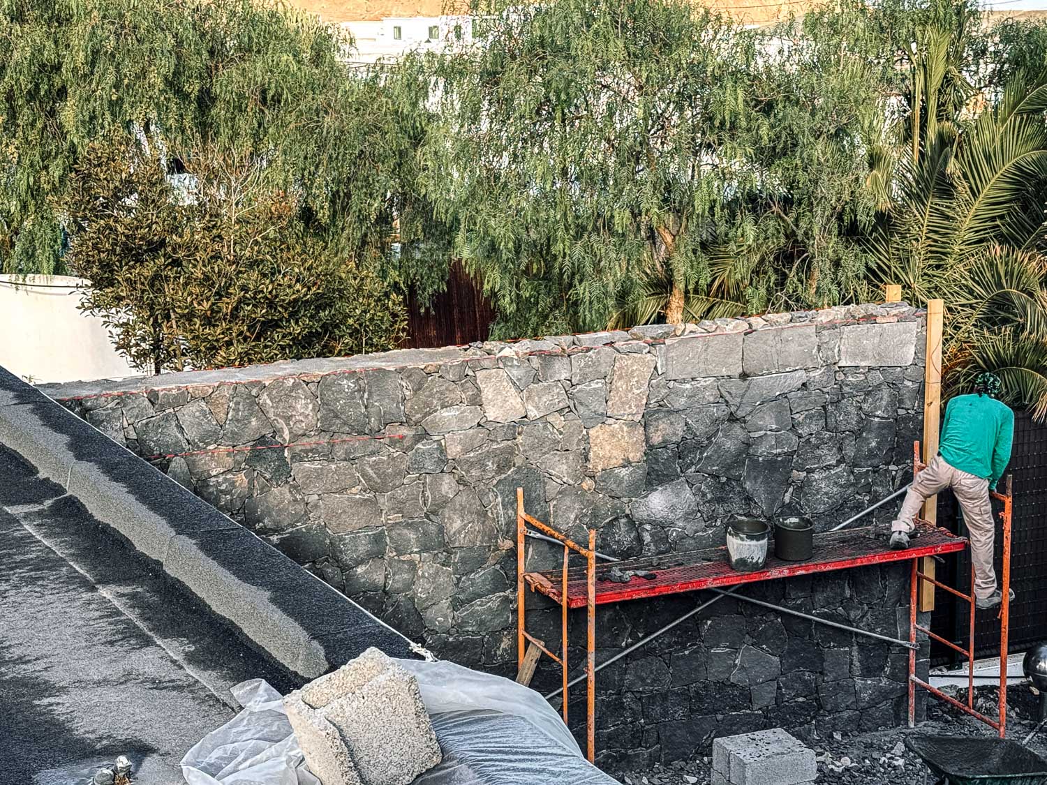 Řemeslník na červeném lešení nanášející omítku na lávovou kamennou zeď, pohled z výšky