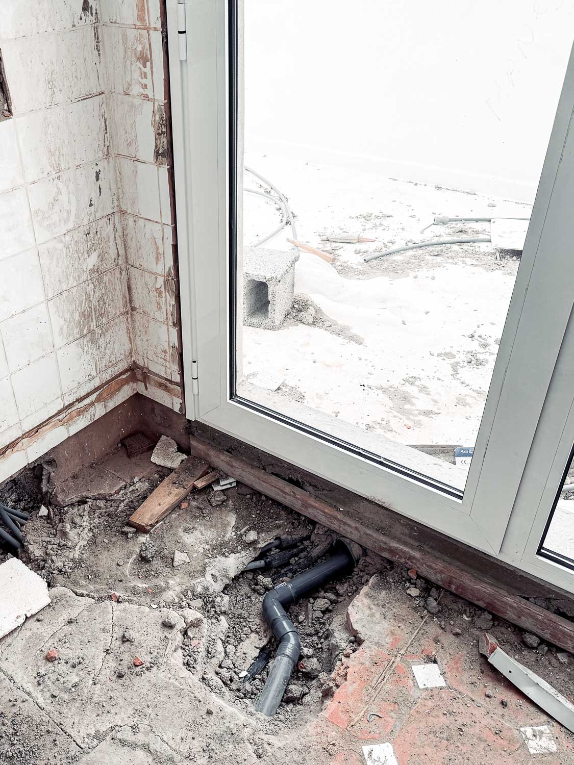 Demolice interiéru – odkrytá instalatérská potrubí skrz rozebranou podlahu u základny okna