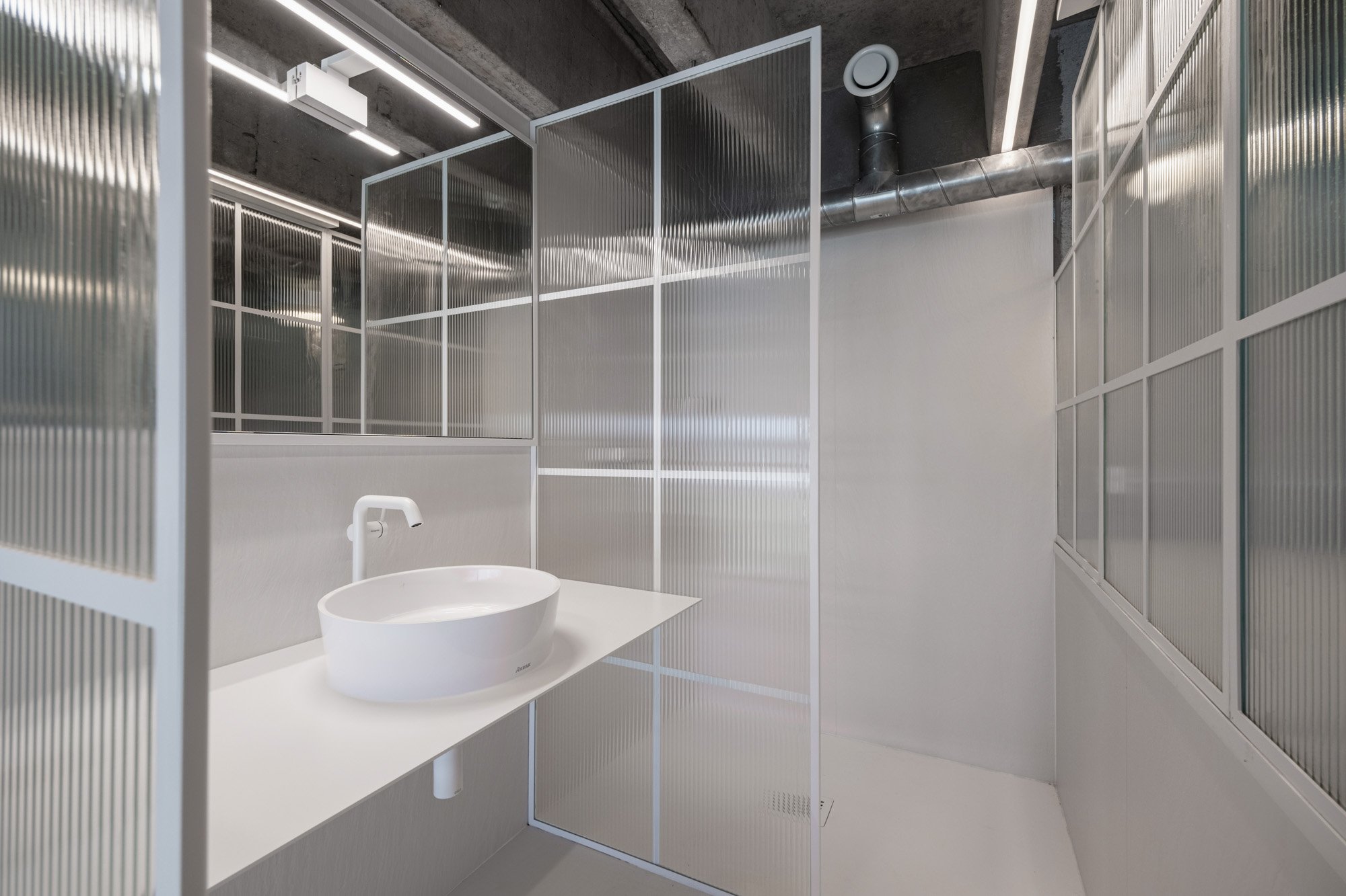 Moderní koupelna se sprchovým koutem za crittall příčkou z rýhovaného (ribbed) skla — bílé nádobové umyvadlo a čisté bílé stěny