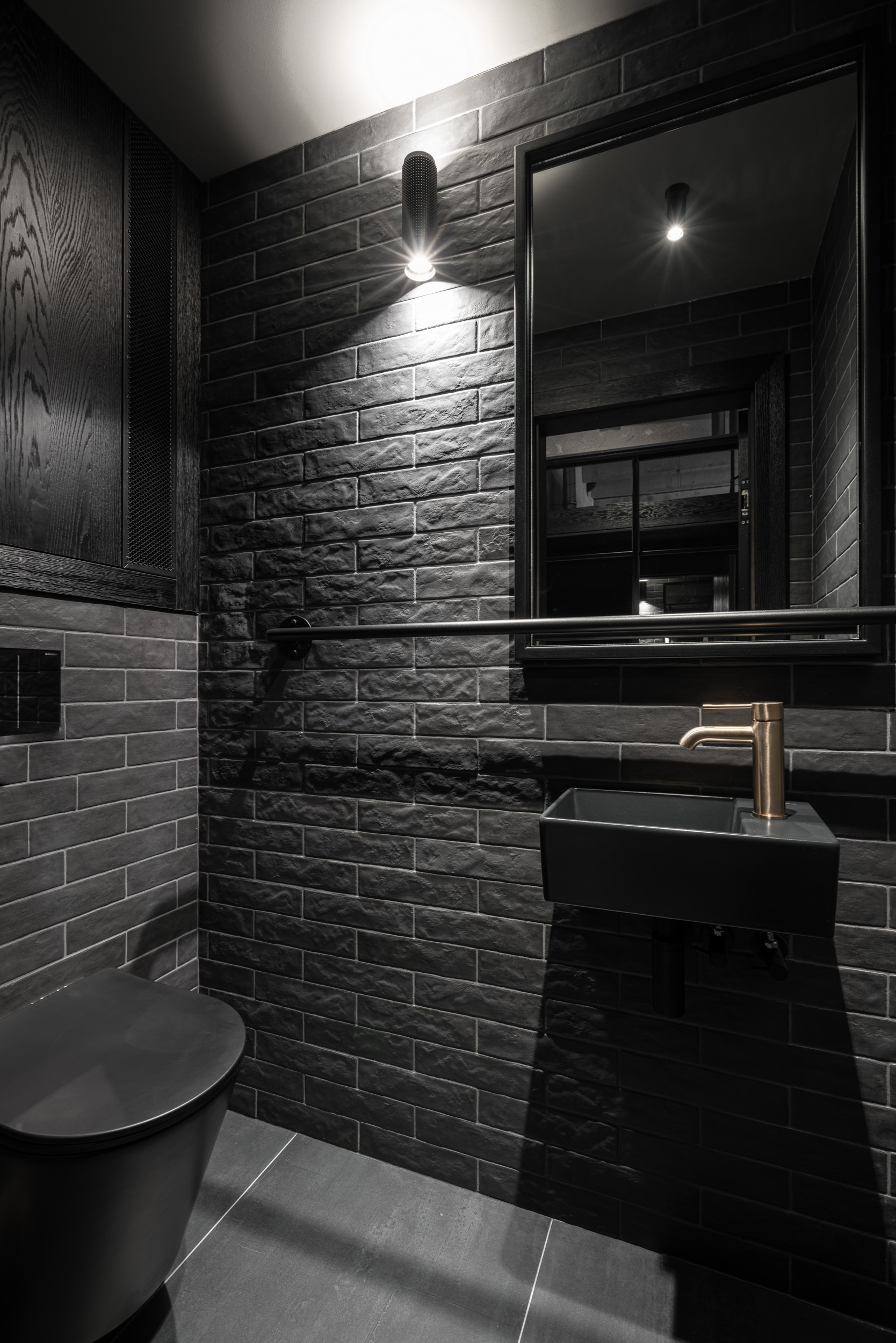 Tmavé WC loftu Vanguard: černé závěsné WC, tmavé Archtiles obklady a mosazná baterie | OOOOX