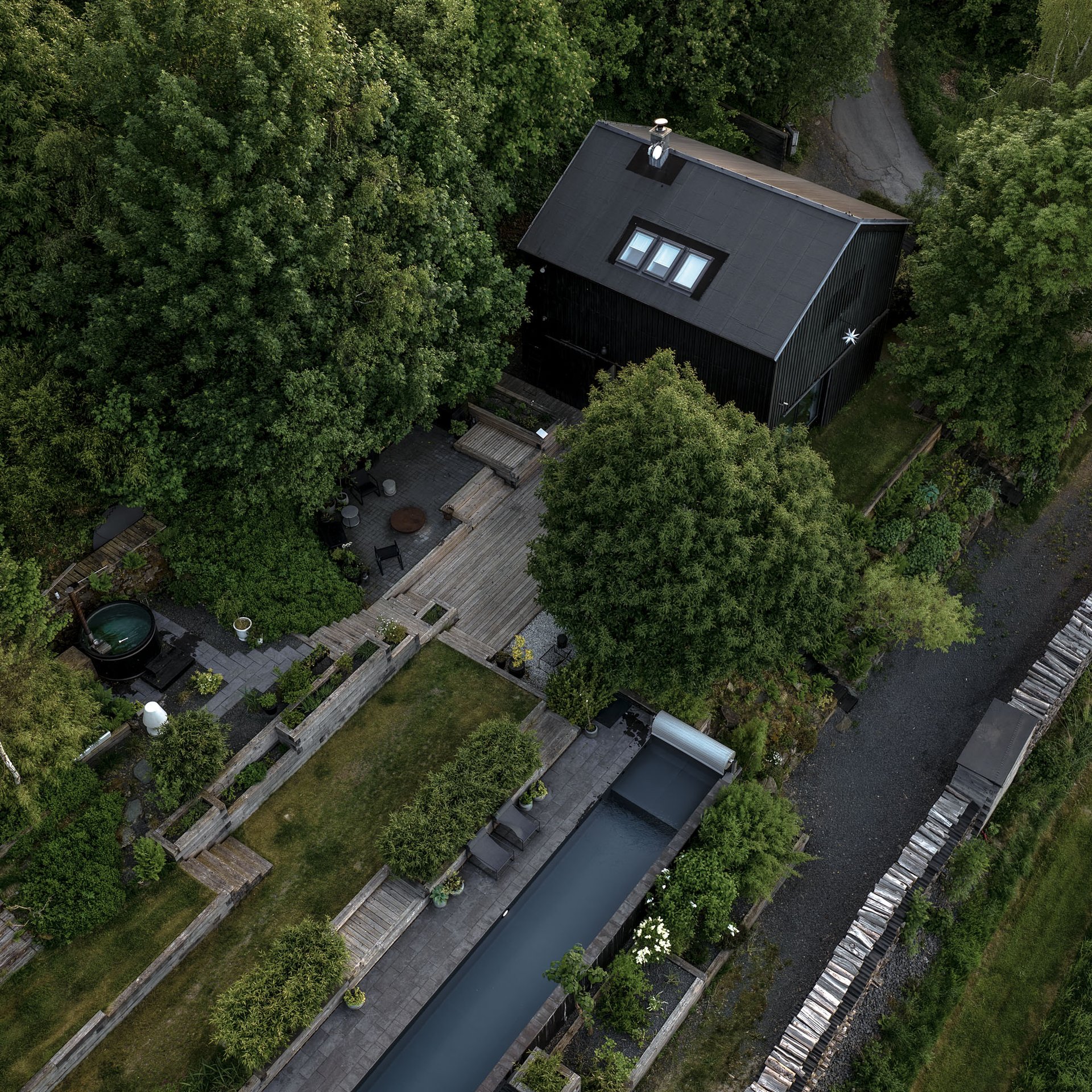 BOX barn conversion — black vertical timber cladding, large panoramic window, garden slope with stacked logs, pool on the slope | OOOOX