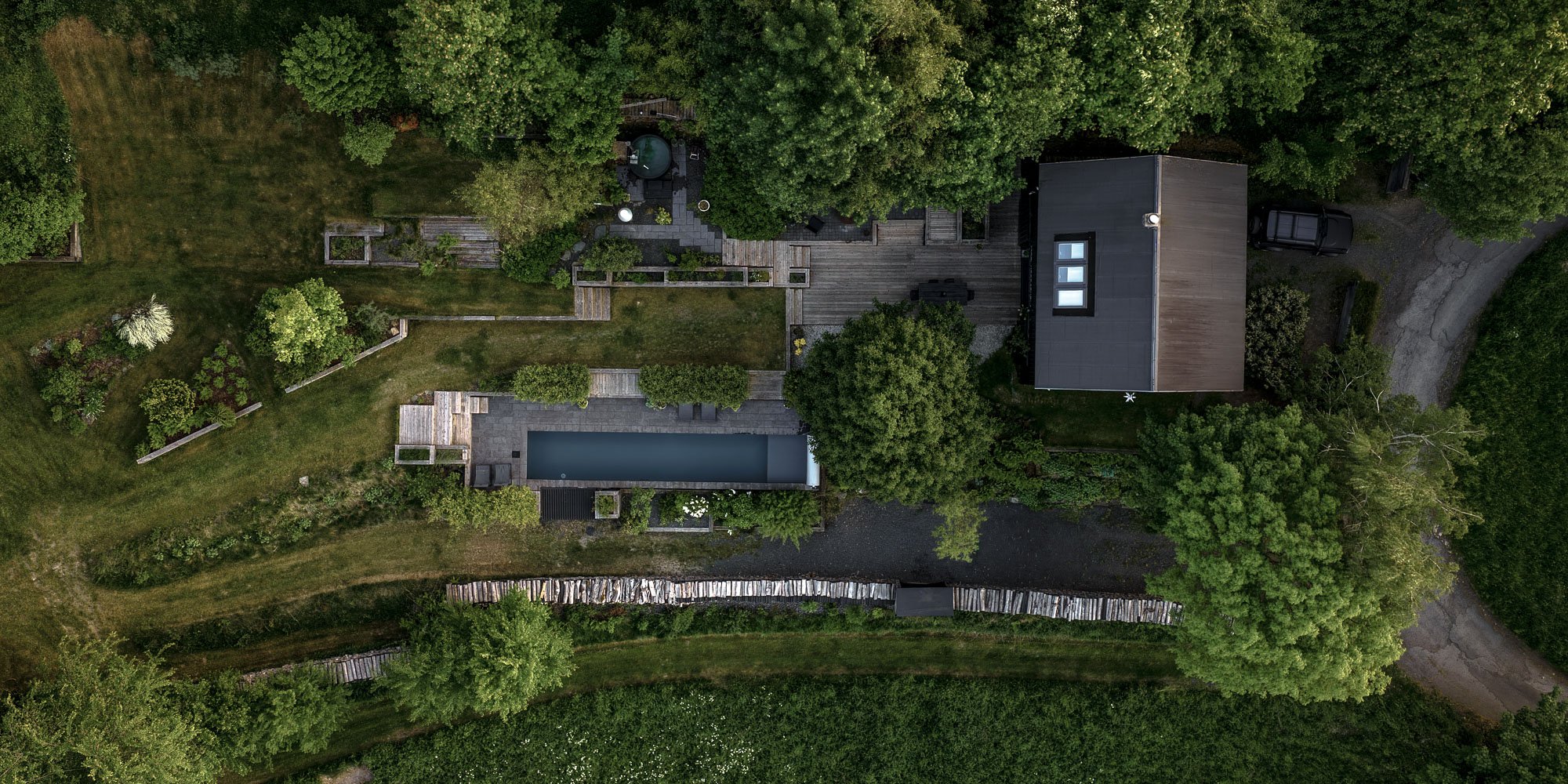 BOX barn conversion — black vertical timber cladding, large panoramic window, garden slope with stacked logs, pool on the slope | OOOOX
