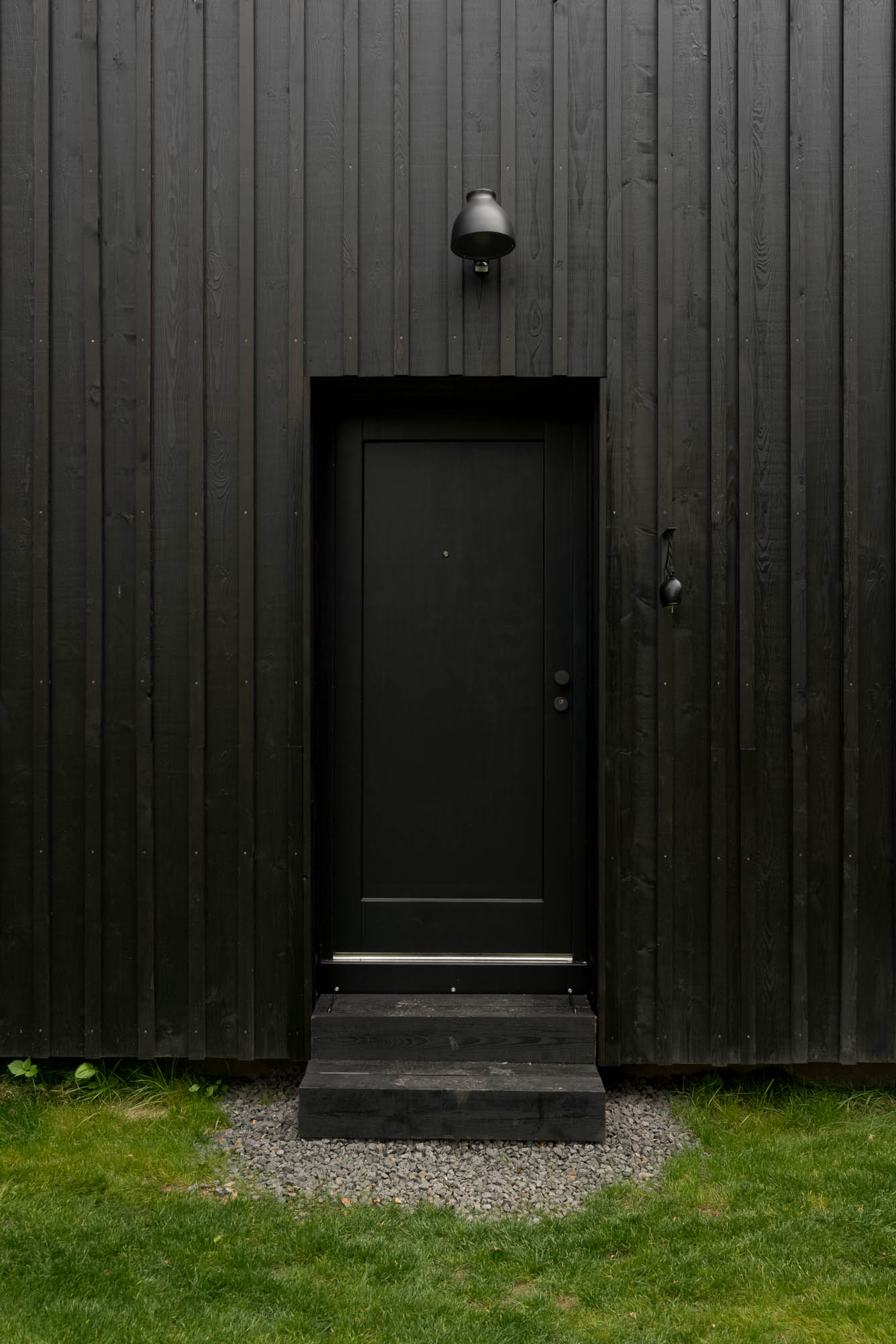 BOX black barn entrance door — black wooden door with black wall lamp above, dark vertical timber facade cladding | OOOOX