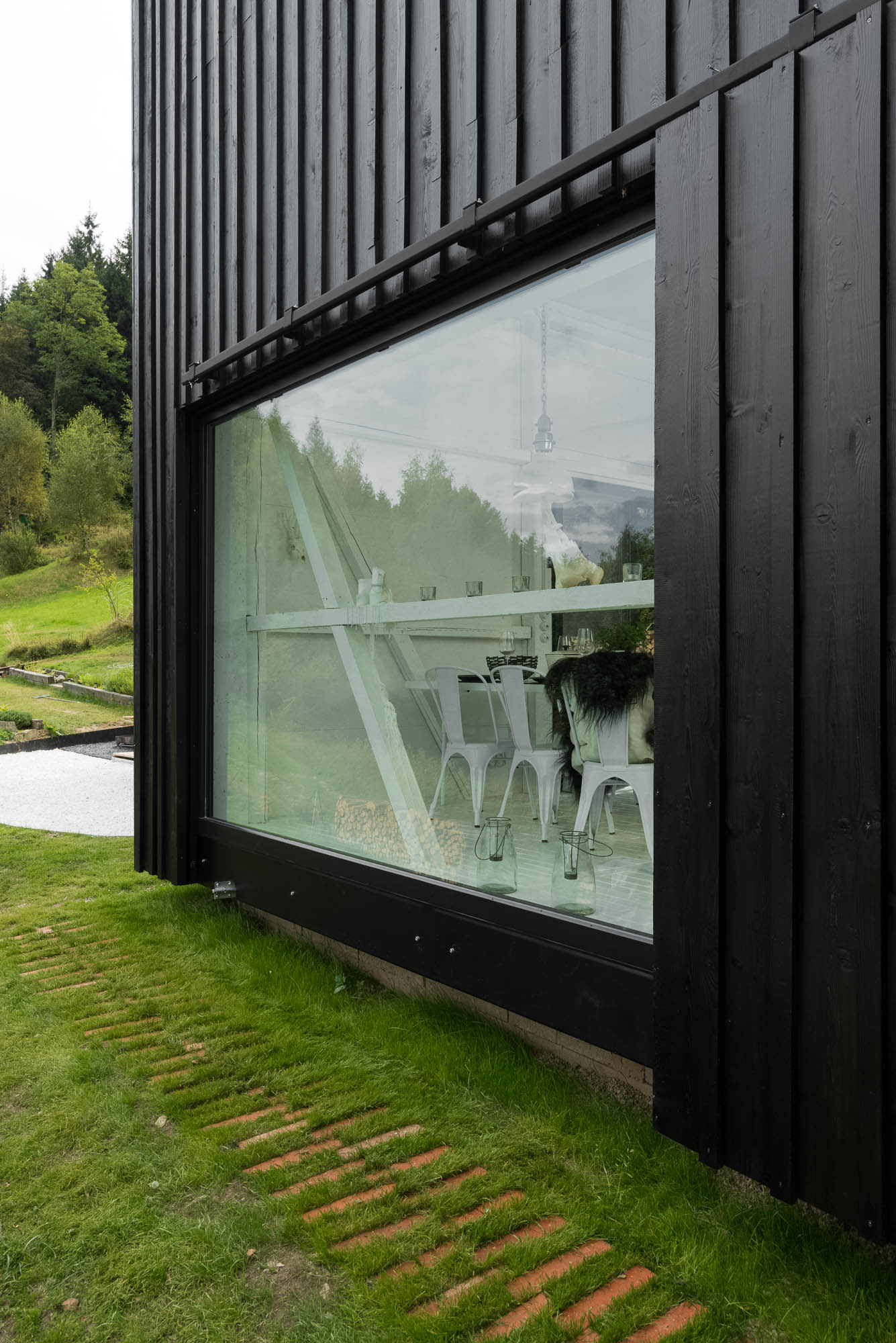 BOX black barn conversion — large panoramic window revealing white dining interior with structural diagonal brace, countryside landscape | OOOOX