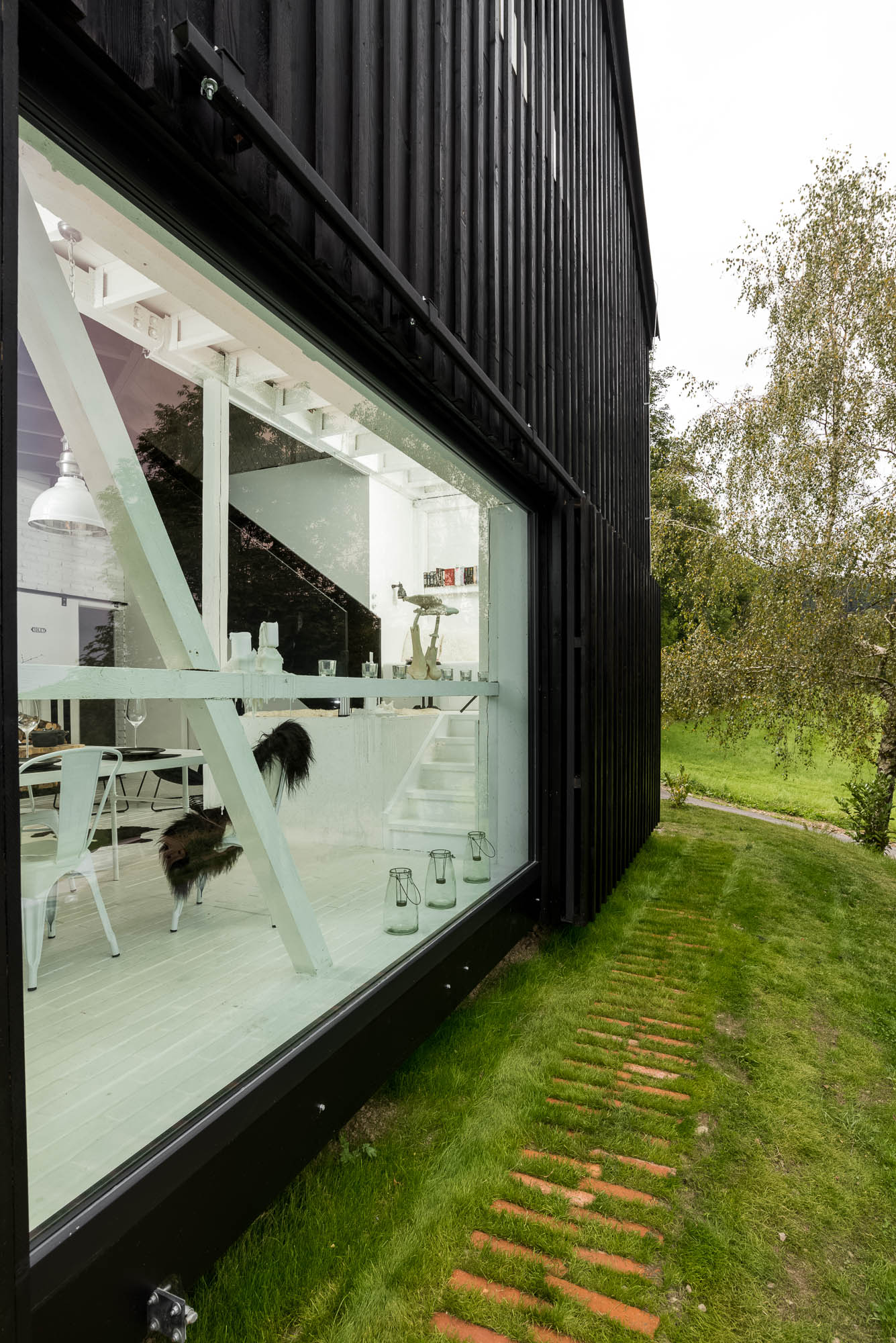 BOX barn conversion exterior — black timber facade with large window, white interior with staircase visible, sloped lawn with brick path | OOOOX