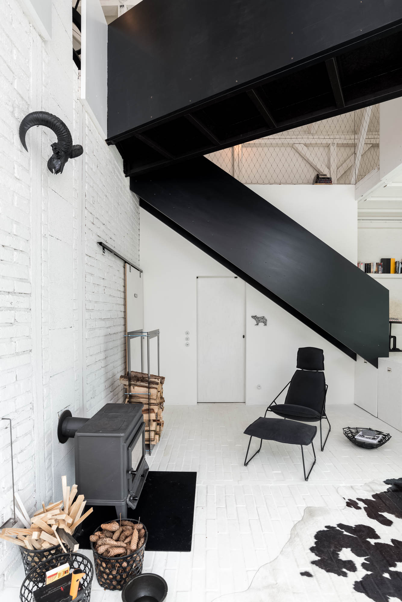 BOX barn living zone — wood stove with firewood, black staircase, wire mesh gallery railing, black designer lounge chair | OOOOX