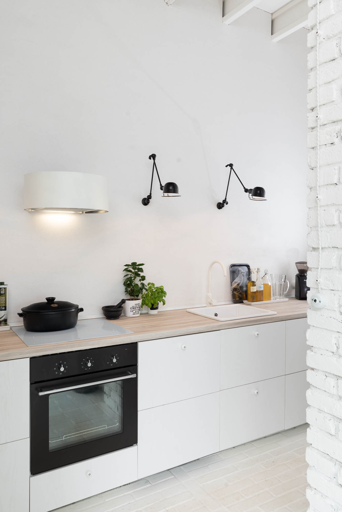 BOX barn kitchen detail — white lower cabinets with oak worktop, black built-in oven, two black articulated wall lamps, white brick column | OOOOX