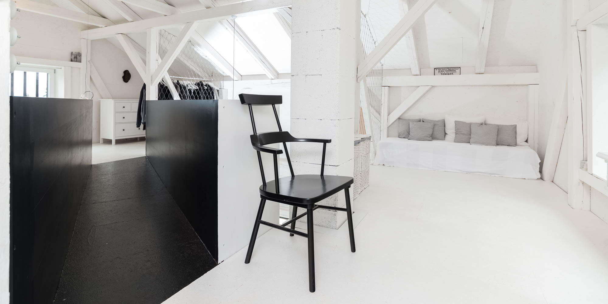 BOX barn upper gallery — black Windsor armchair, double bed with grey linen bedding, white roof trusses, wire mesh railing, open dressing area | OOOOX