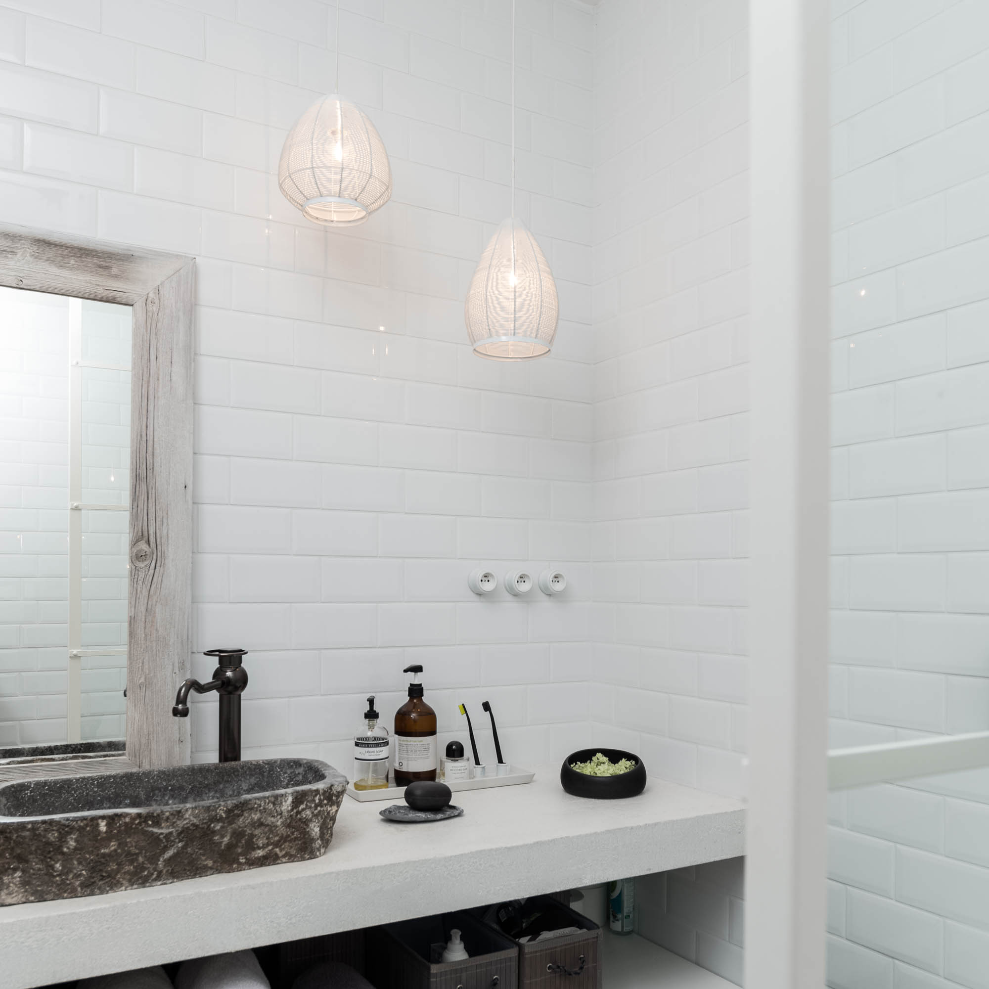 BOX barn bathroom vanity — stone river rock vessel sink on white concrete countertop, dark bronze tall faucet, weathered wood-framed mirror, white wire pendant lights | OOOOX