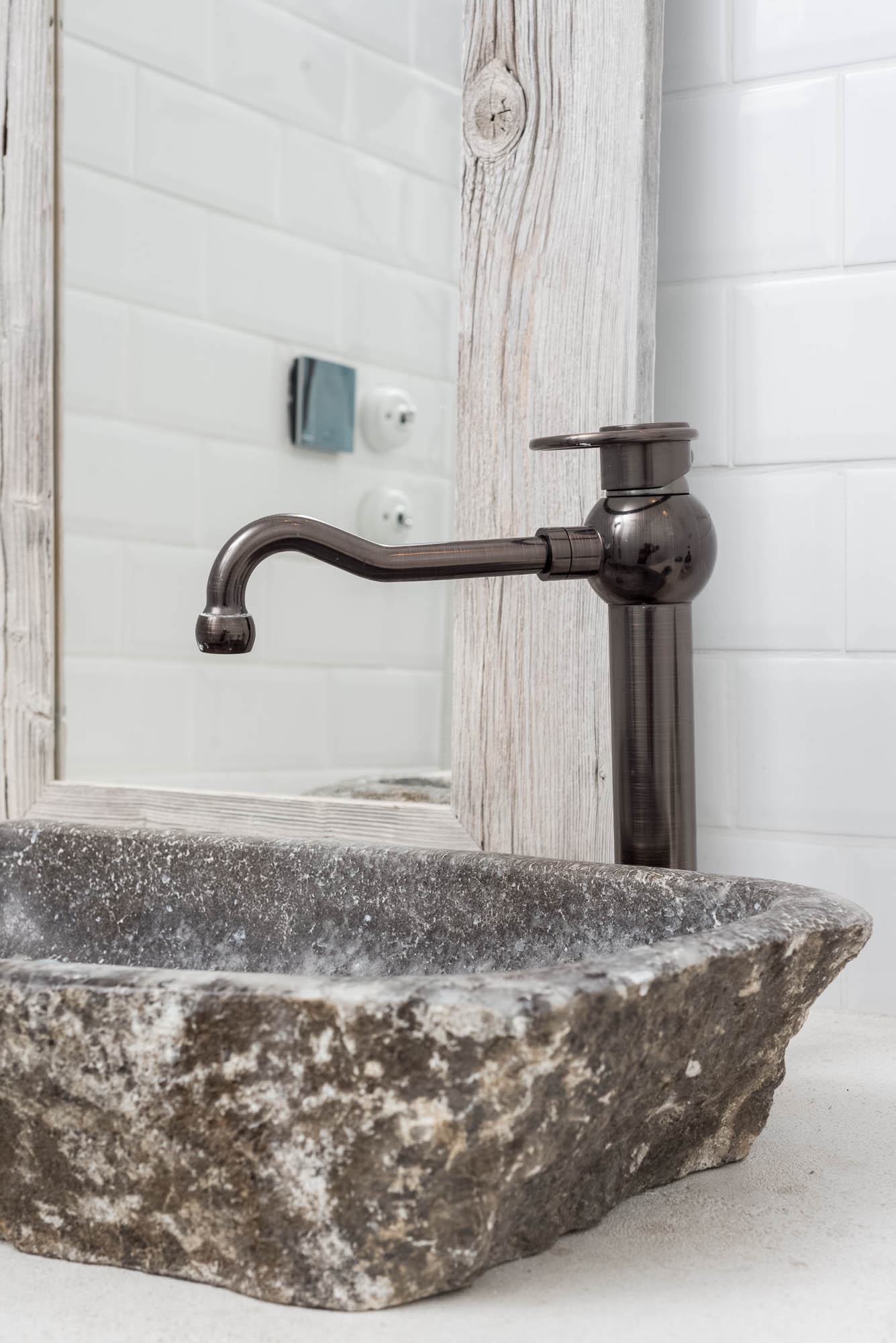 BOX barn bathroom detail — stone vessel sink with dark bronze faucet, weathered wood mirror frame, white subway tile wall | OOOOX