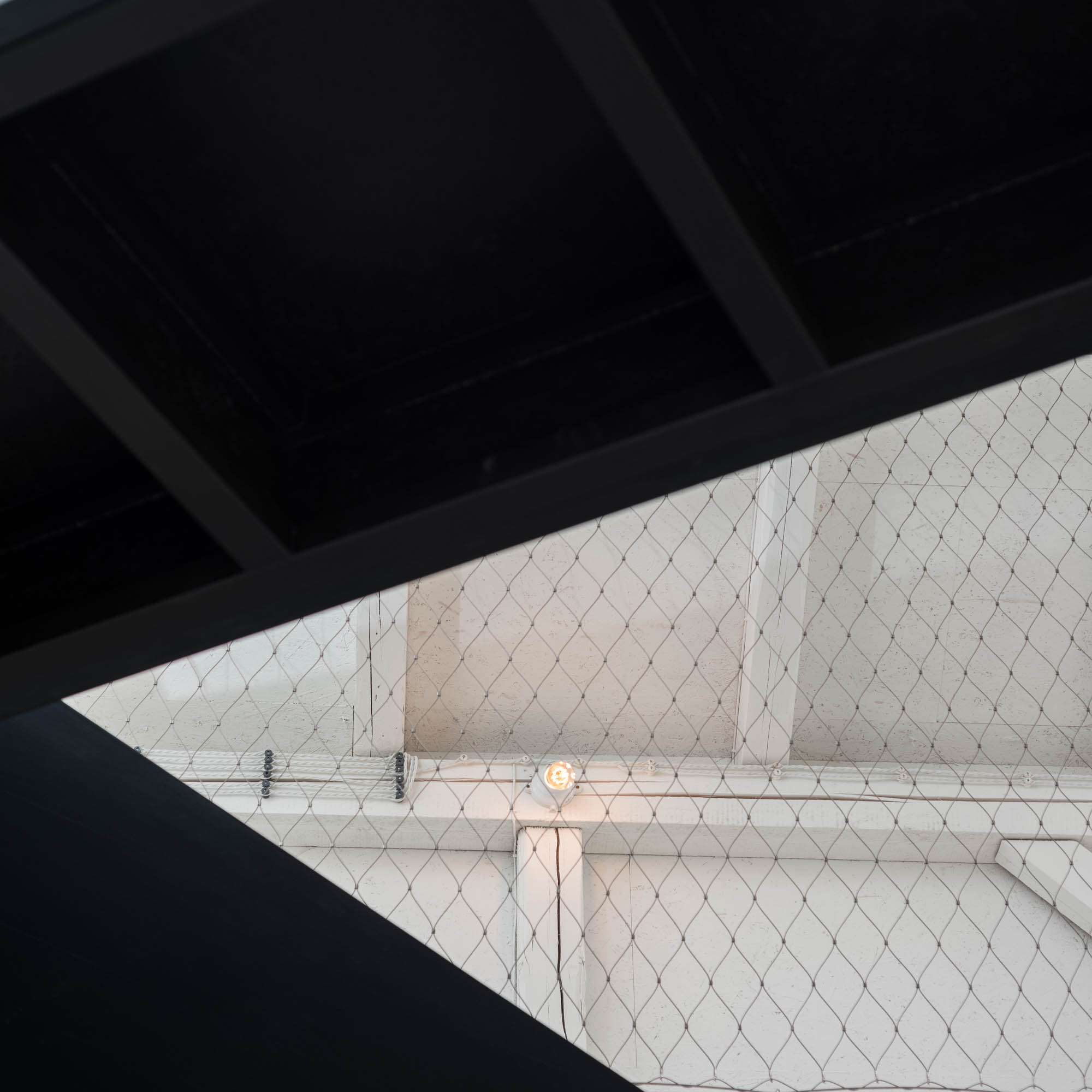 BOX barn abstract architectural detail — view from below of black steel staircase meeting white wire mesh gallery railing, graphic black-and-white composition | OOOOX