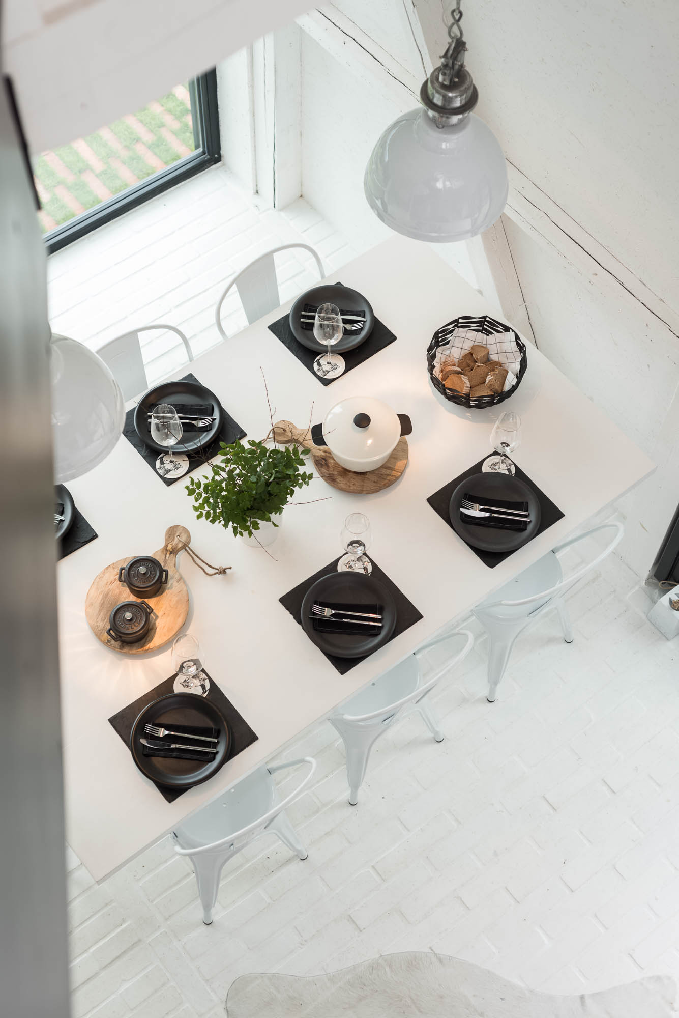 BOX barn dining table from above — black place settings, cast iron pot on wooden board, white Tolix chairs, industrial pendant lights viewed from gallery | OOOOX
