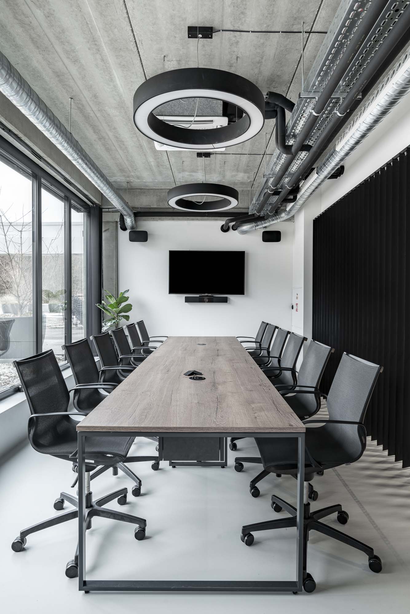 Moderní zasedací místnost v industriálním kancelářském interiéru s betonovou podlahou, minimalistickým nábytkem a přiznanými technologiemi. Design by OOOOX
