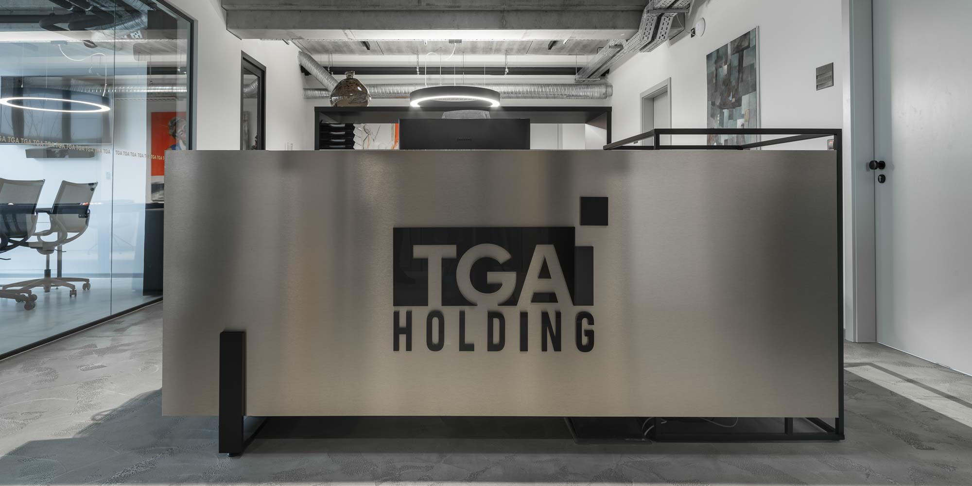 Recepční prostor kanceláří TGA holding propojený s otevřeným pracovním prostorem, betonovými konstrukcemi a dominantním ocelovým schodištěm. Design by OOOOX