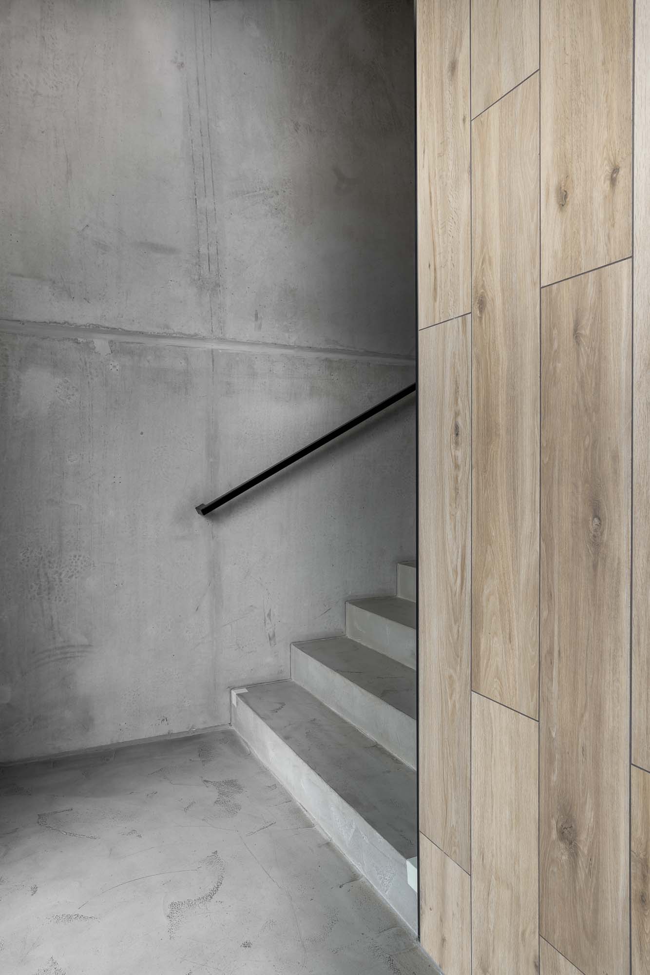Detail napojení betonového schodiště na vestavěný nábytek ze světlé dýhy v moderním industriálním interiéru kanceláří TGA holding. Design by OOOOX
