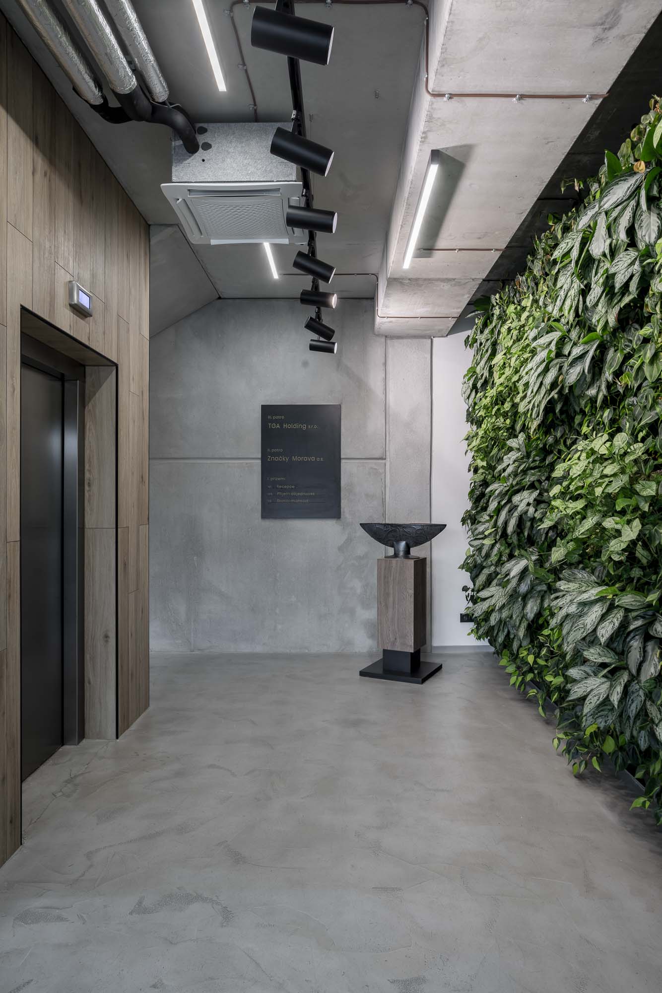 Výtahová zóna se zelenou stěnou, betonovou stěrkou na podlaze a stěnách a minimalistickým industriálním řešením kancelářského interiéru. Design by OOOOX