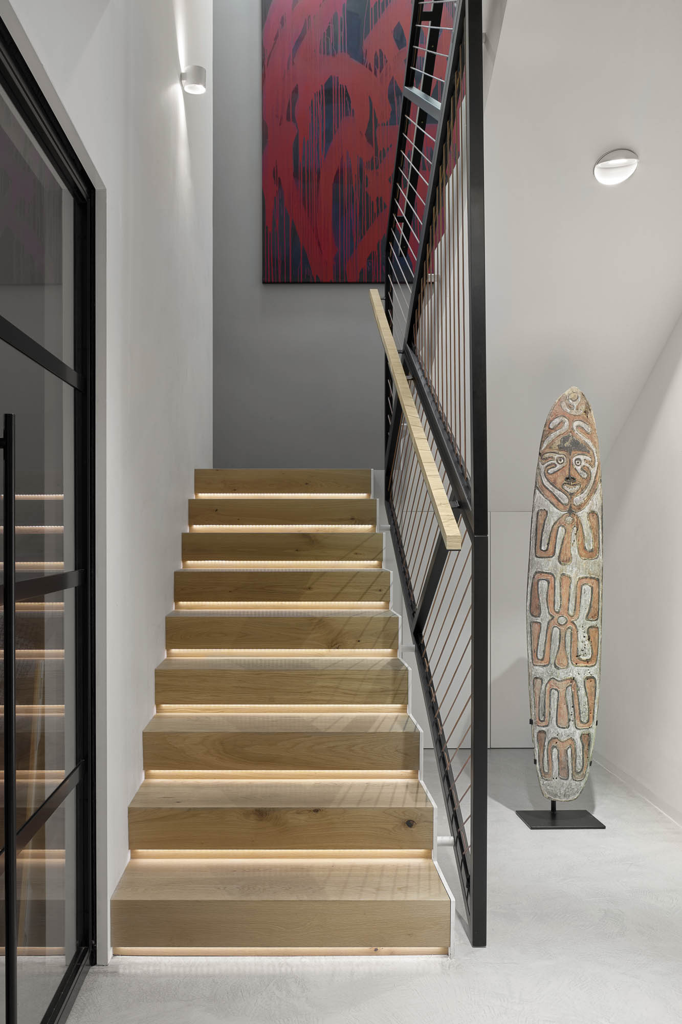 Schodiště s dubovými schody s LED podsvícením, černé ocelové zábradlí s koženými lany a kmenová skulptura | OOOOX