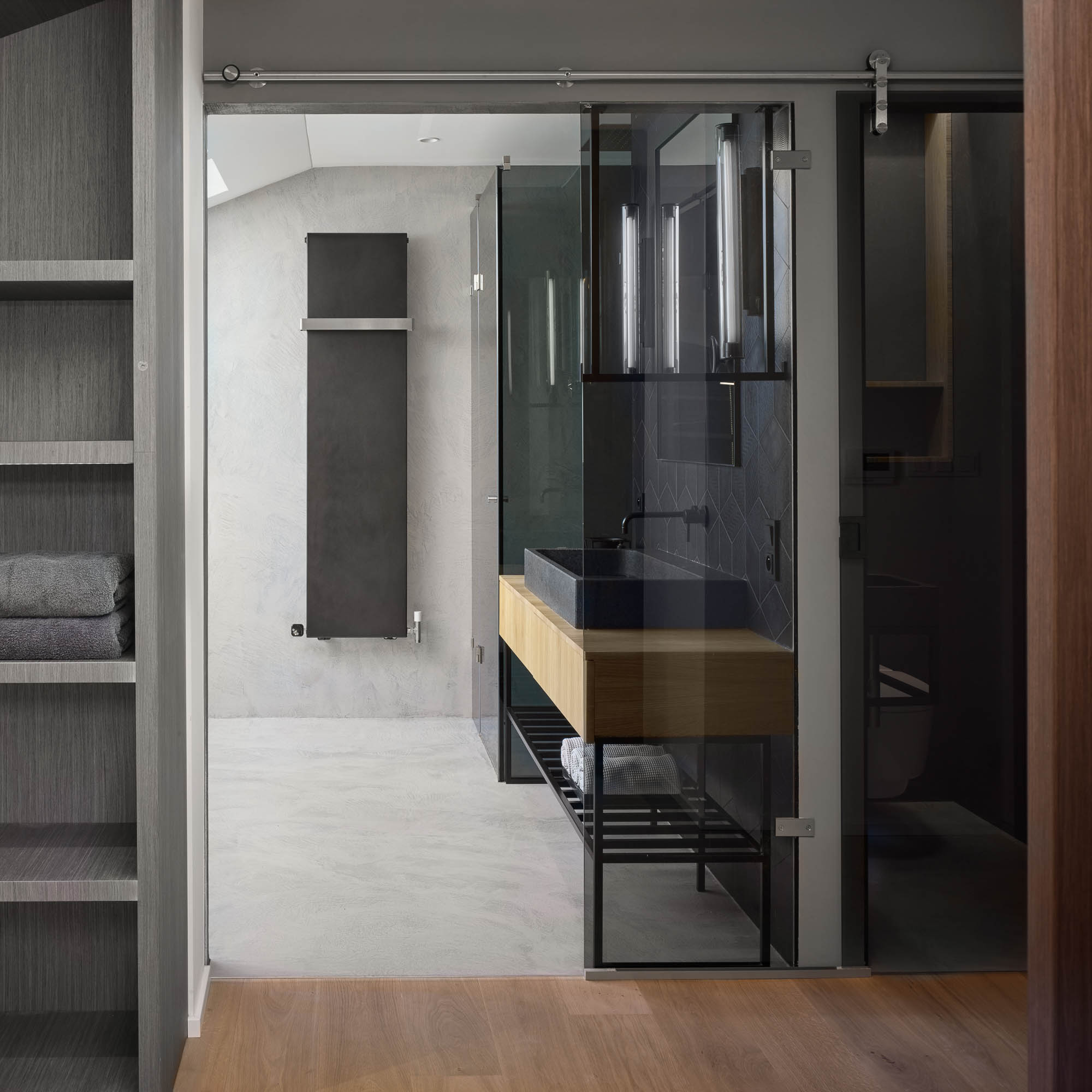 Wardrobe view into bathroom stone vessel sink oak vanity dark geometric ceramic tile vertical LED lights OOOOX