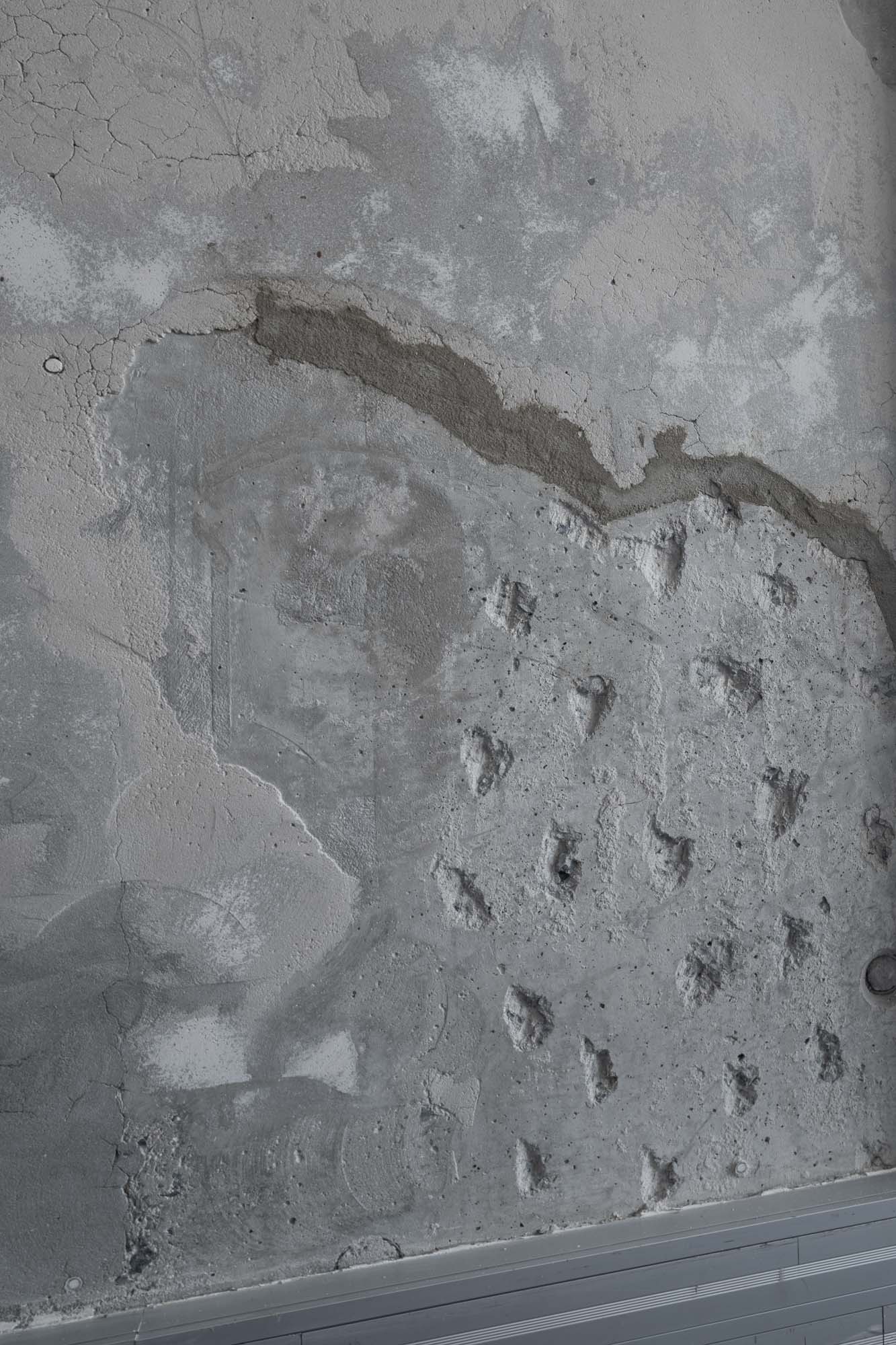 Makro detail surového pohledového betonového povrchu stropu v kancelářích Cybex Praha; těžce texturovaný beton s otisky původního bednění, trhlinami, záplatami a vrstvami historické úpravy z budovy z 90. let