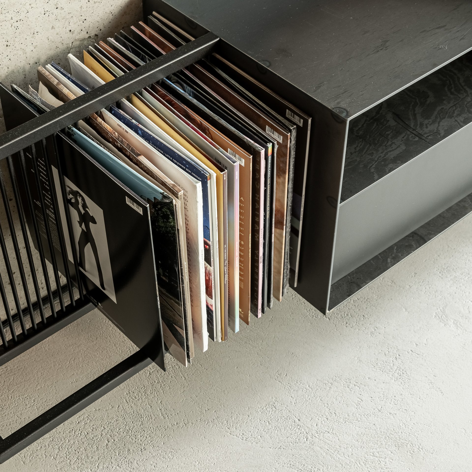 Detail stojanu na vinylové desky vily Hřebenky – zakázkový černý ocelový stojan s LP deskami uloženými ve slotech, deska z tmavého kamene viditelná v pozadí
