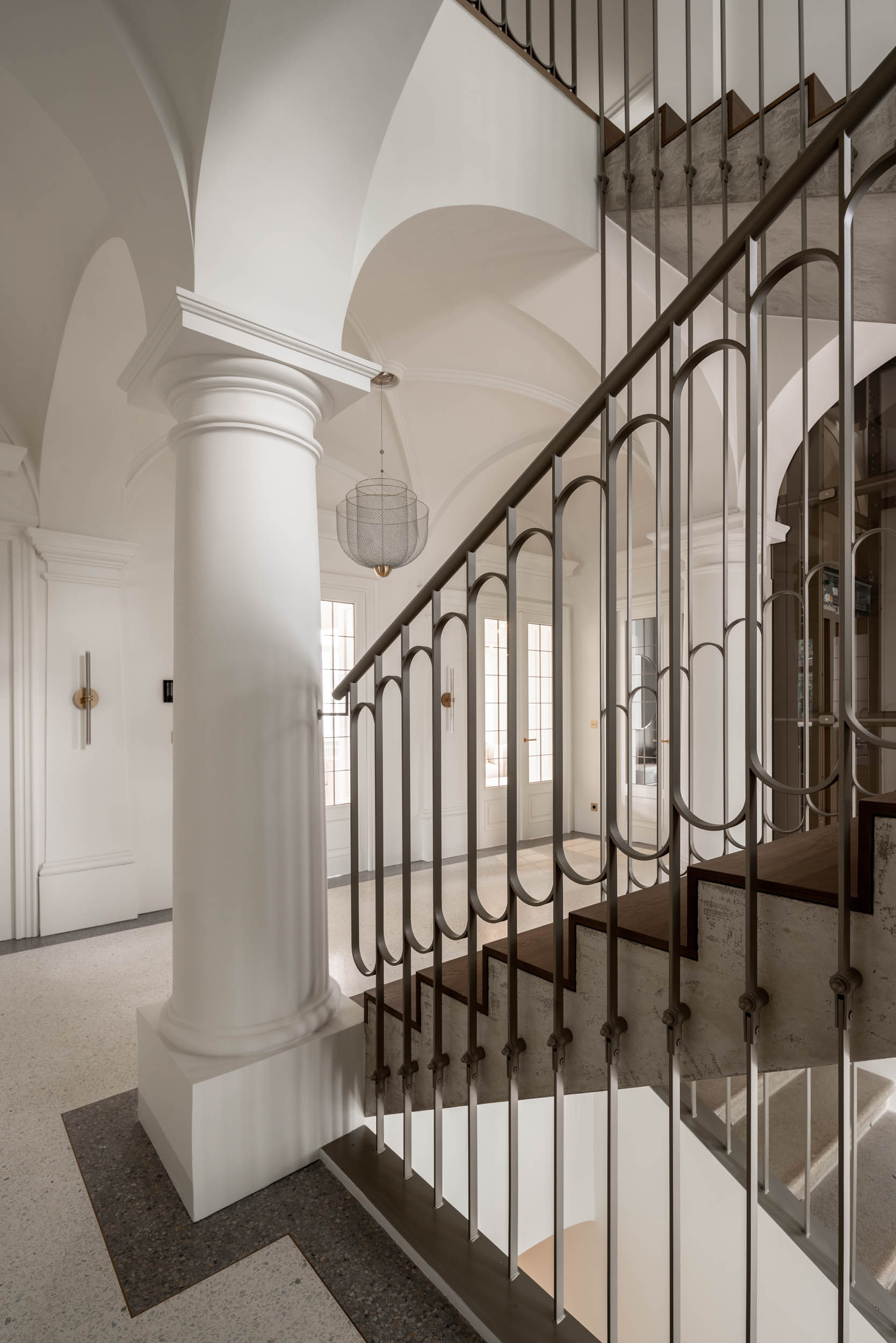 Detail of the entrance hall with the original exposed vault, new terrazzo flooring with a brass frame, light wire chandelier and new concrete staircase – luxurious atmosphere | design by OOOOX