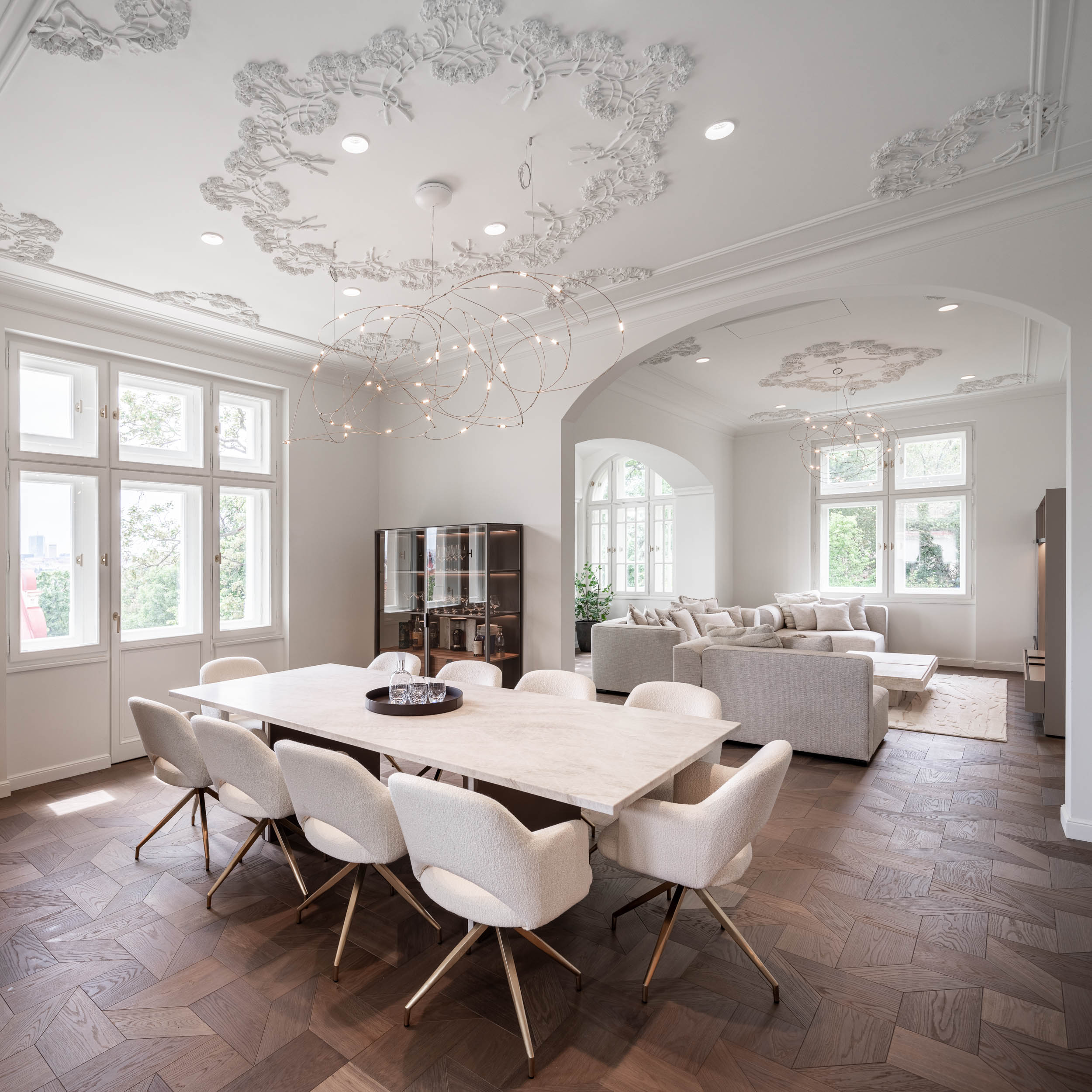 Dining table with white upholstered chairs, American walnut parquet flooring and generous stucco ceilings in the minimalist interior of Villa Vinohrady by OOOOX