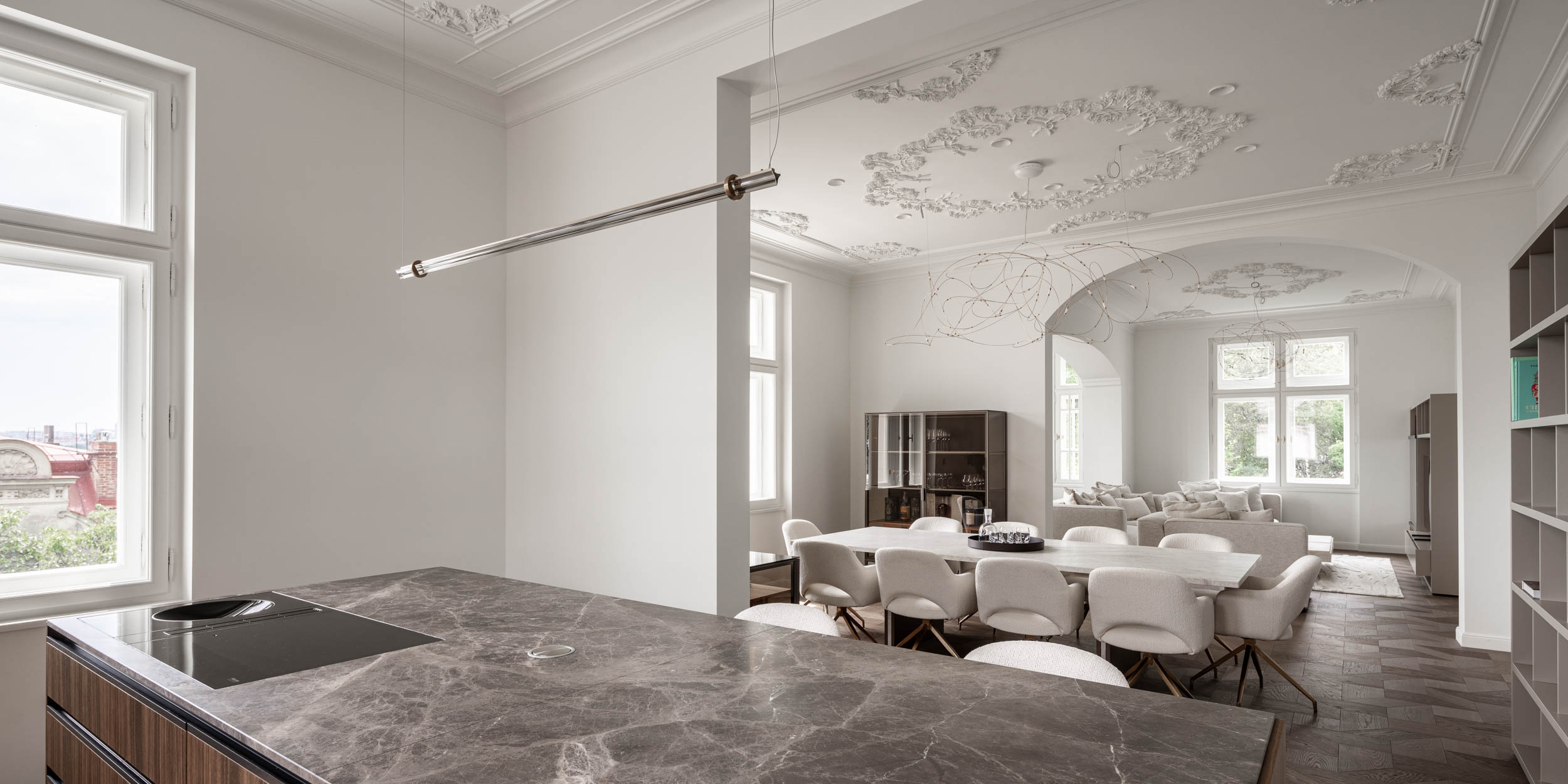 View of the dining and living area from the serving kitchen within the open space of Villa Vinohrady, stucco ceilings and custom American walnut parquet flooring | design by OOOOX