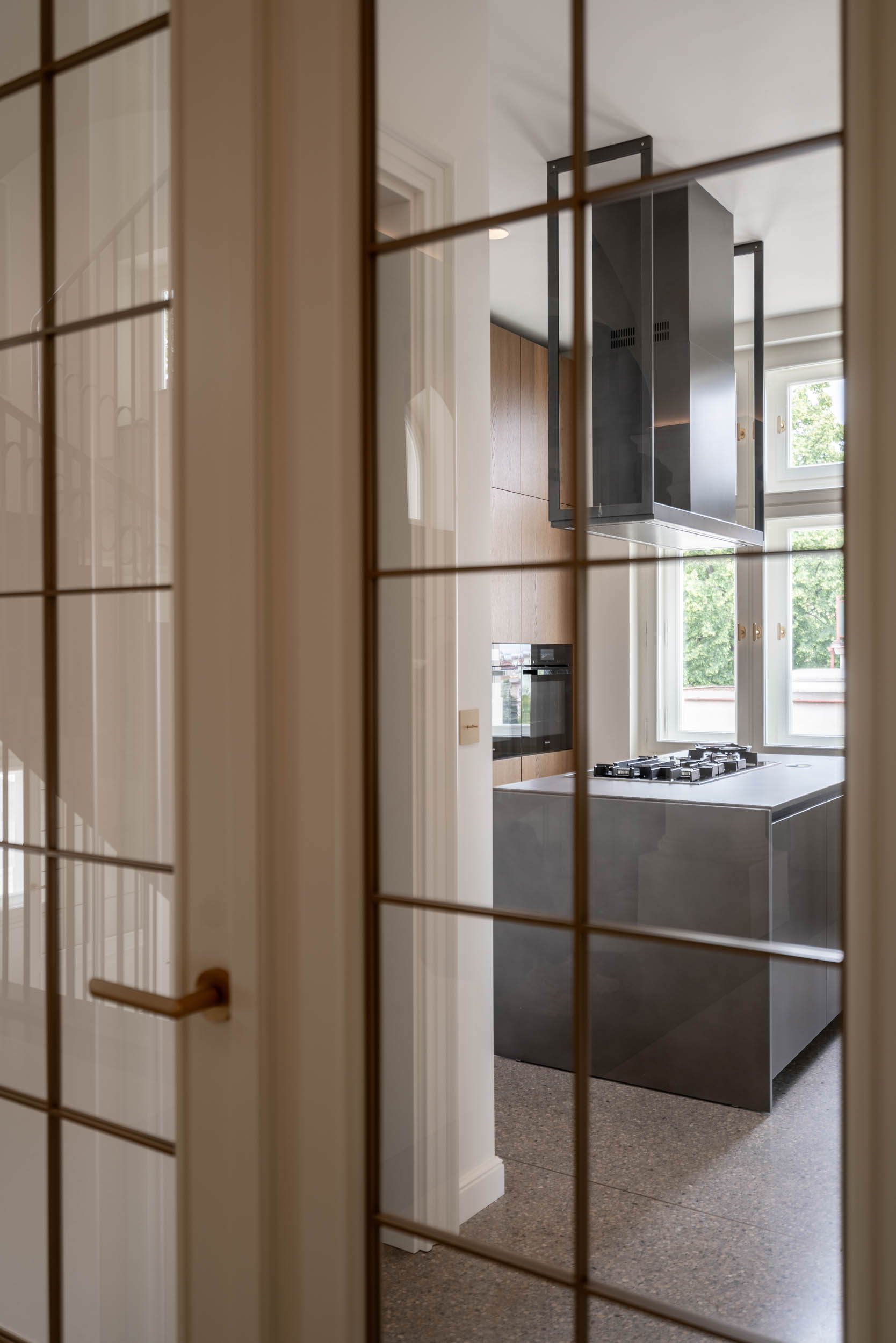 View through glazed double doors into the working kitchen with an island and designer extractor hood | villa reconstruction by OOOOX