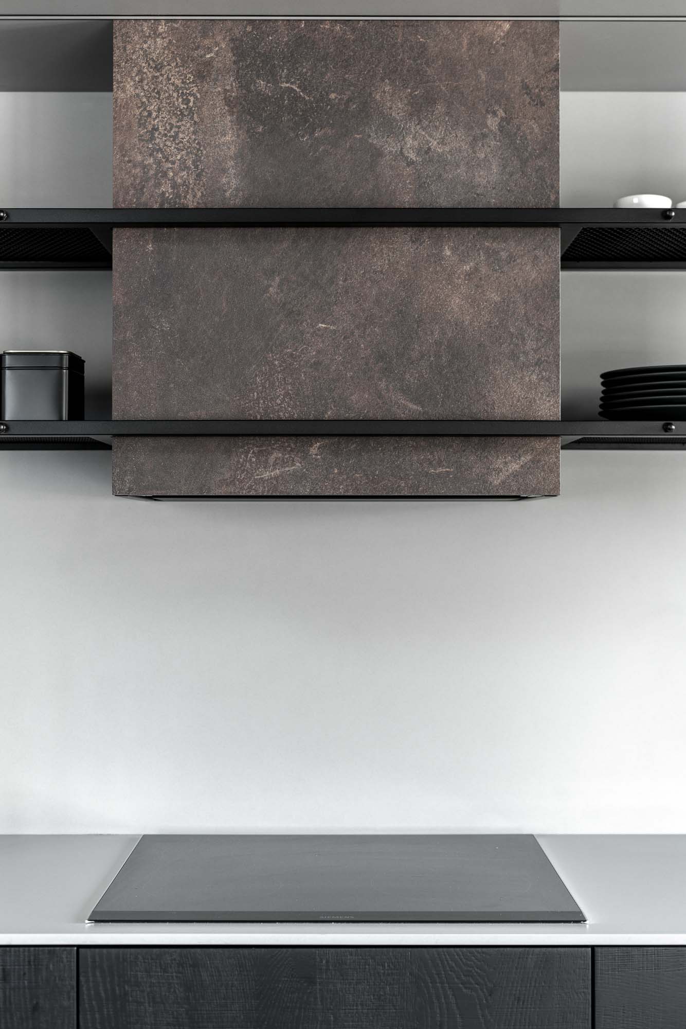 Designová digestoř obložená materiálem v dekoru kortenové oceli v minimalistické kuchyni industriálního bytu Mlýn. Design by OOOOX