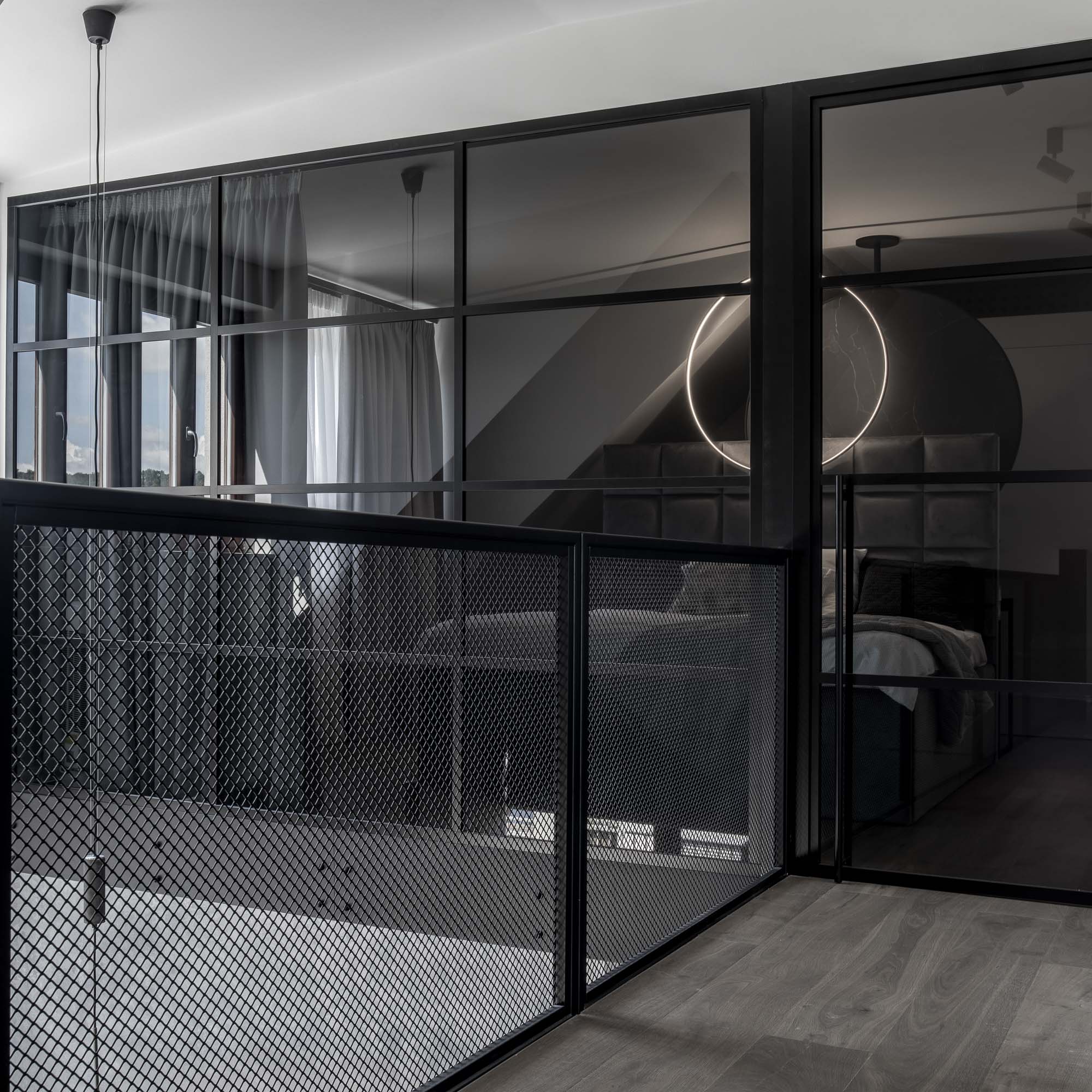 Pohled do ložnice přes ocelovou příčku s kouřovým sklem, otevřený loftový interiér s dubovou podlahou a industriálními detaily. Design by OOOOX