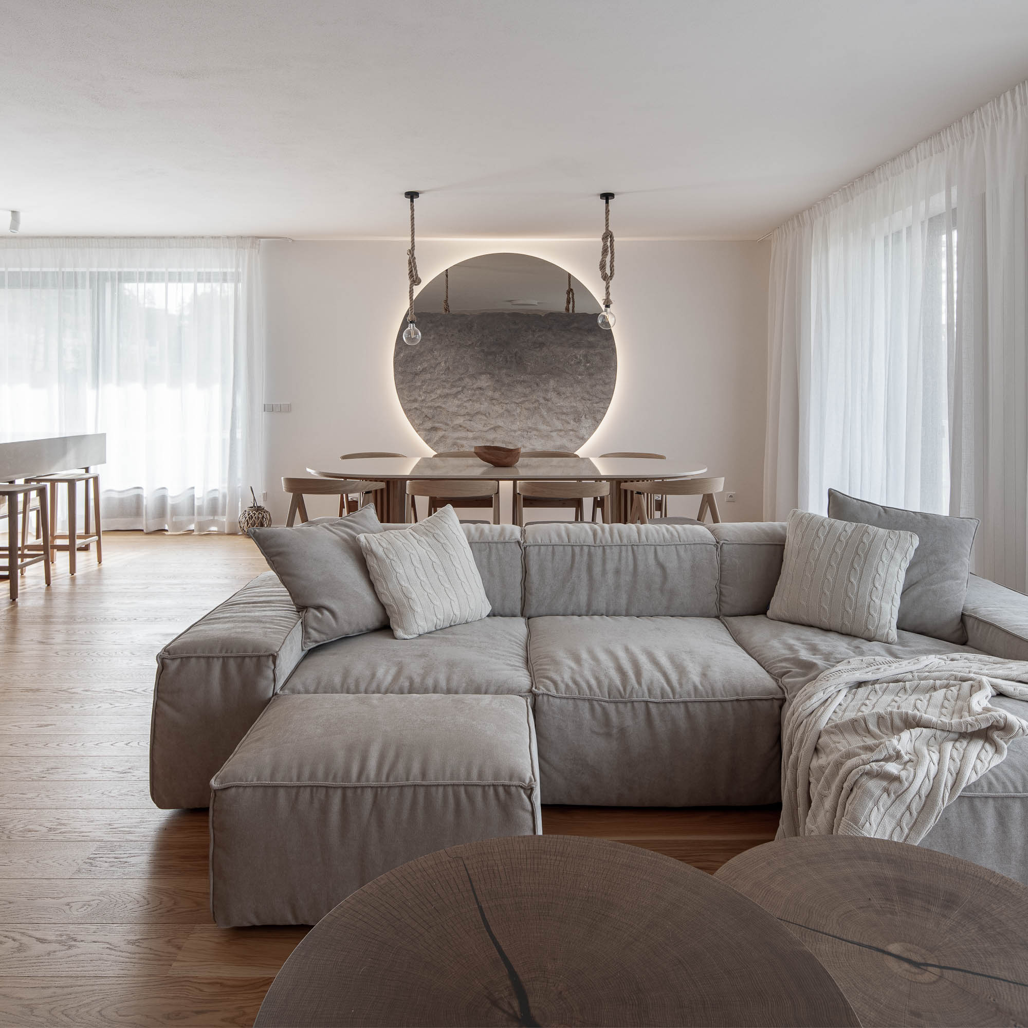 Obývací pokoj apartmánu Lipno s modulární pohovkou, kulatým podsvíceným zrcadlem a jídelním koutem OOOOX Praha