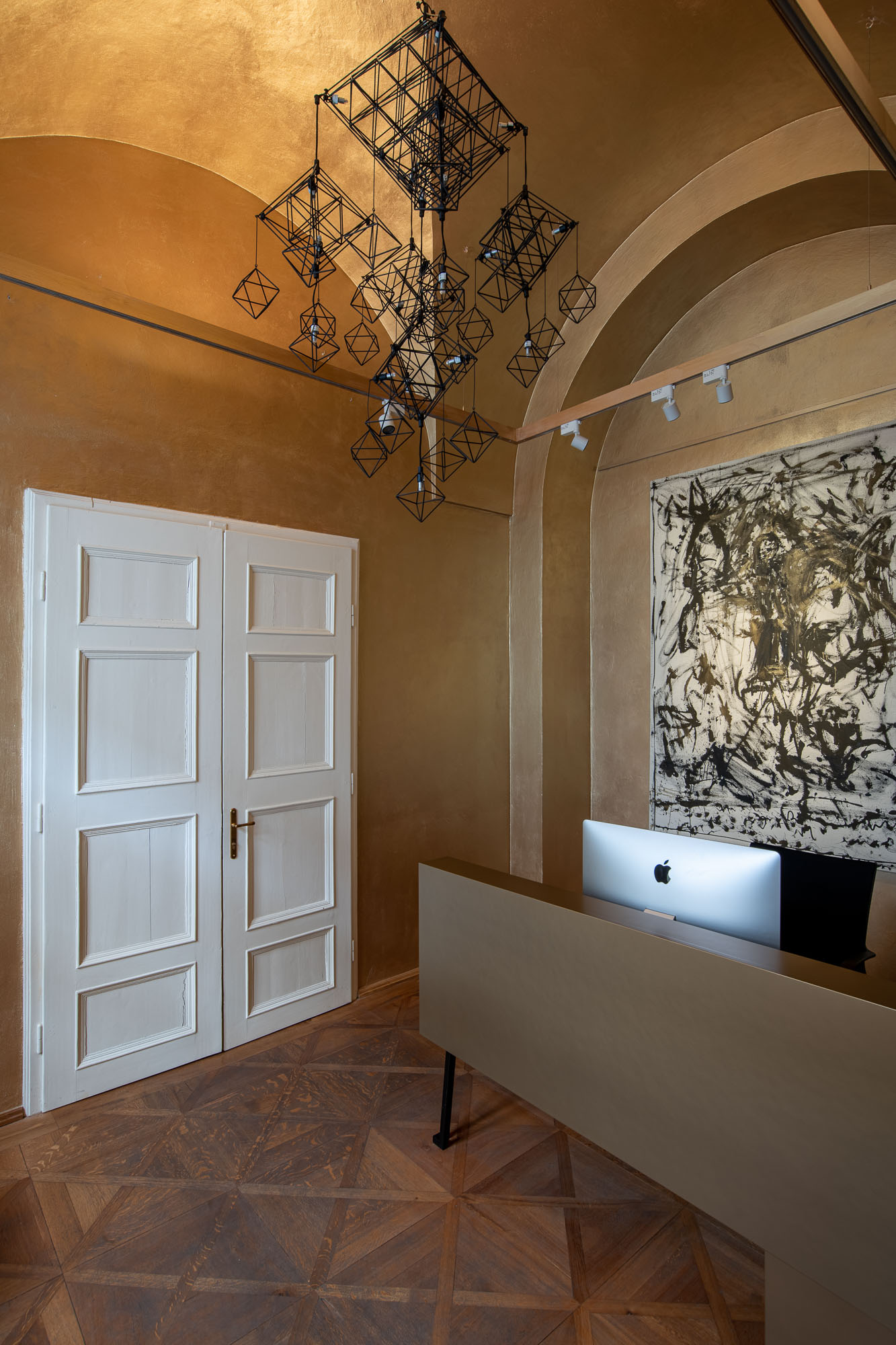 Drátěné geometrické svítidlo v recepci galerie ARCIMBOLDO fotografované zdola. Oktaedrické tvary na zlaté texturované omítkové klenbě.