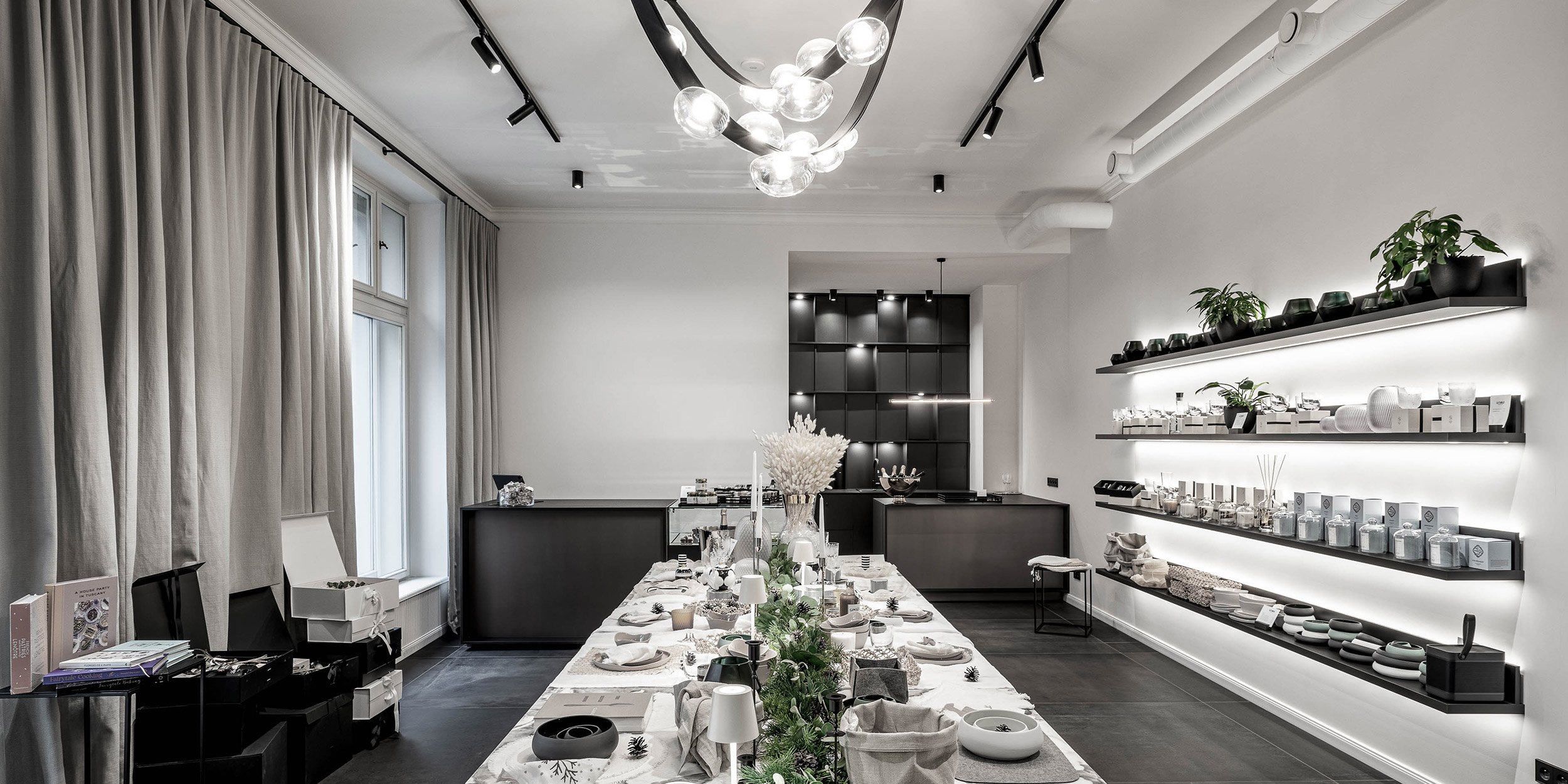 Celkový pohled na showroom LA TABLE s vánočním stylingem stolu — kvartzitový stůl nastrojený k eventu, tmavá mřížková stěna, záříci produktové regály vpravo, organické stropní světlo