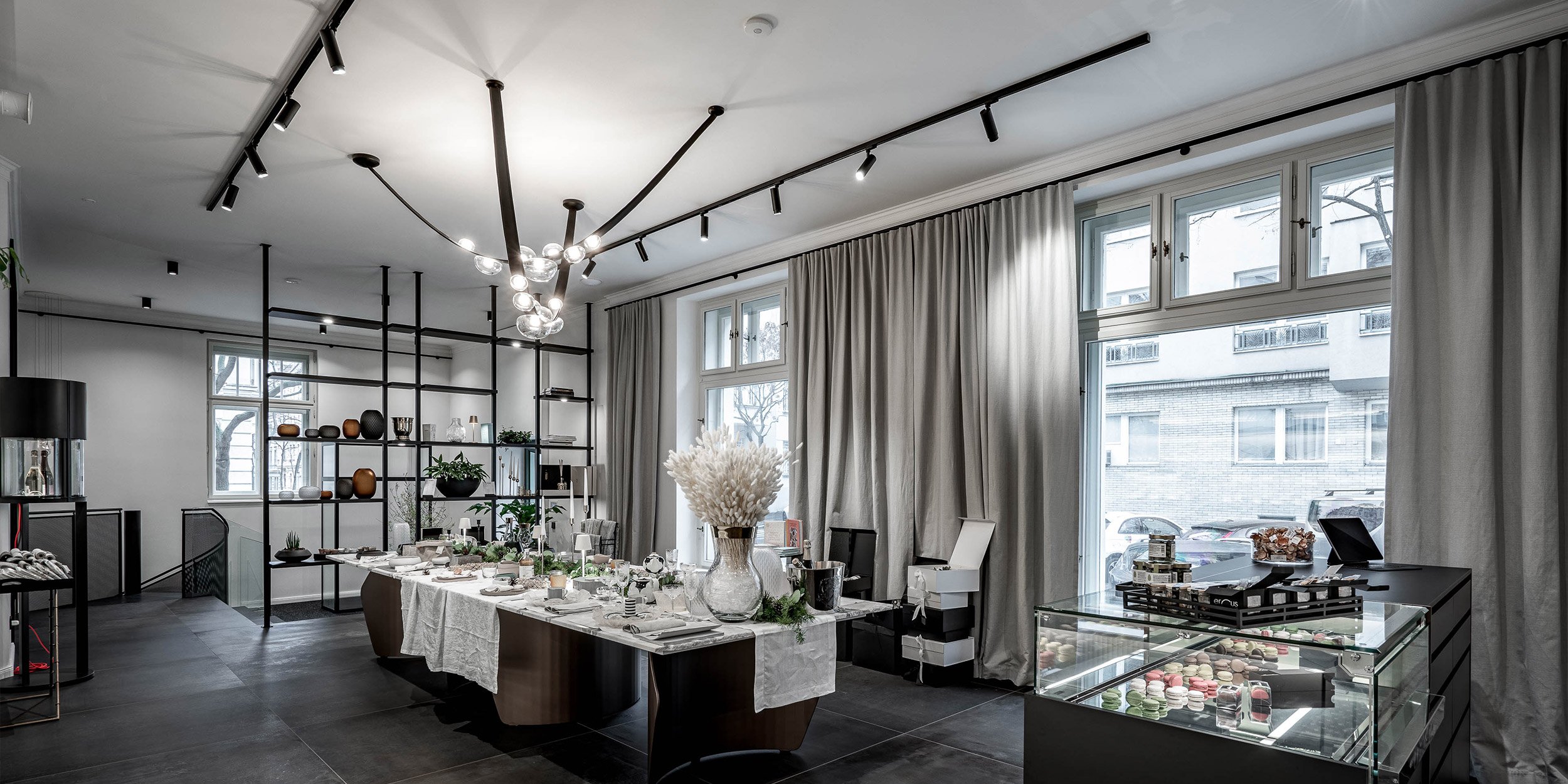 Showroom LA TABLE od vstupu — kvartzitový stůl s vánočním dekorem, ocelový regálový systém vlevo, prosklená vitrína vpravo, výlohy do ulice