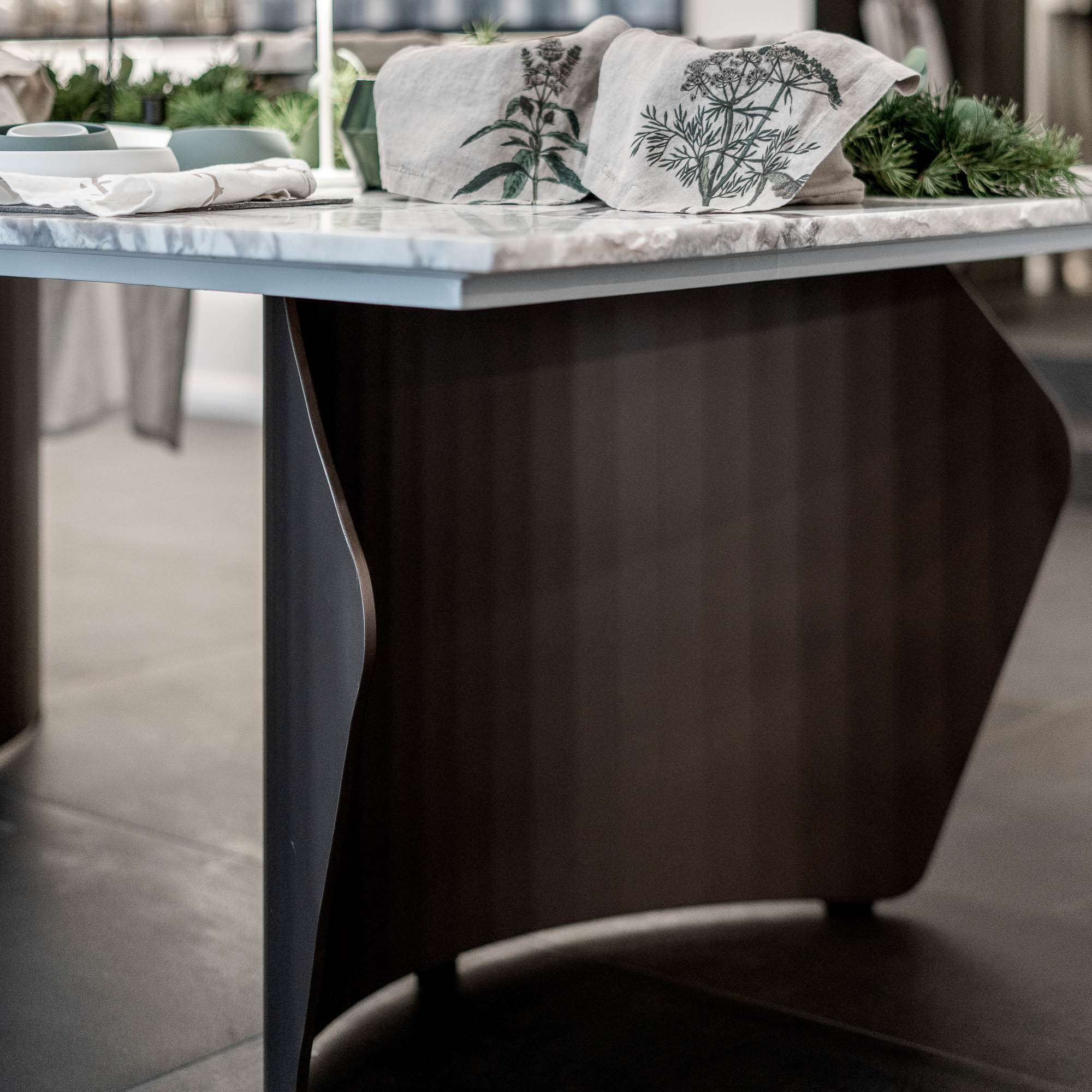 Detail skulpturálního ocelového podstavce kvartzitového stolu LA TABLE — geometrická tmavá ocelová konstrukce, deska z kvartzitu s lněnými ubrousky, event styling v pozadí