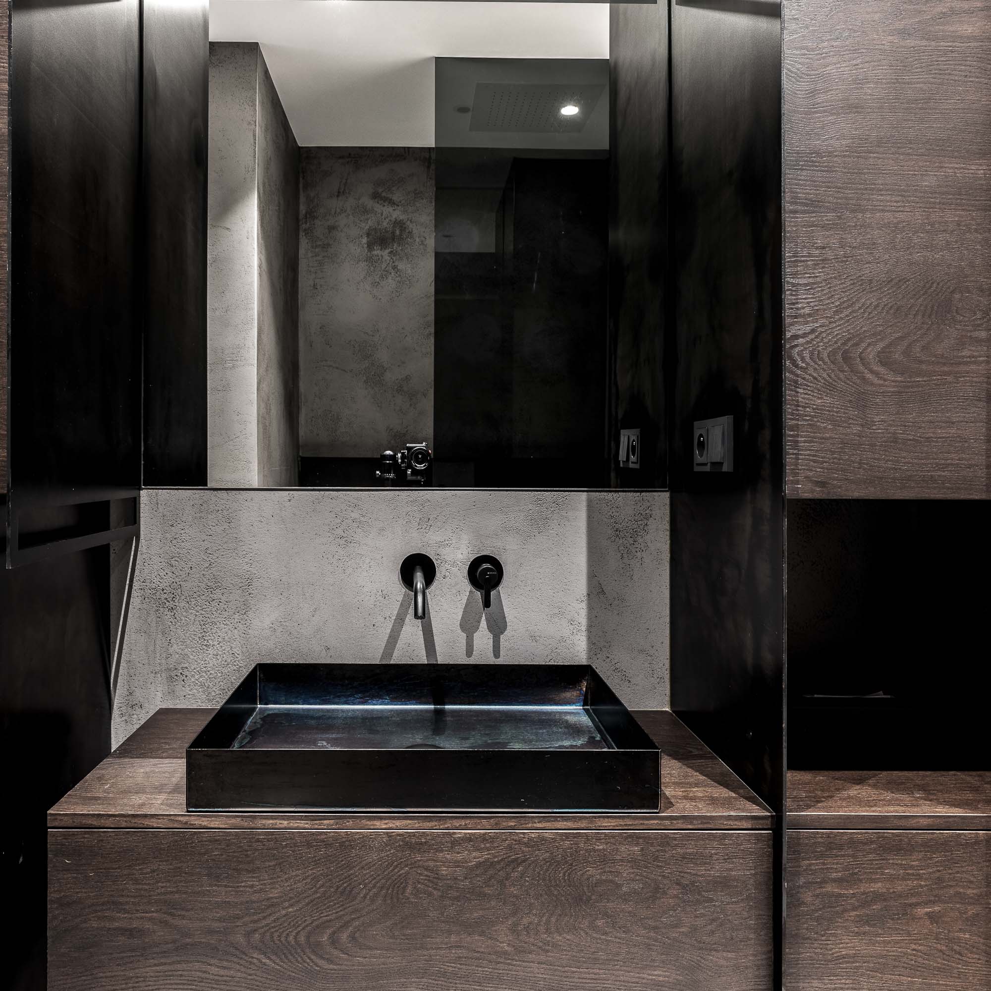 Detail wellness koupelny domu Černošice – zblízka záběr tmavého kamenného umyvadla na tmavém dřevěném vanity s černými nástěnnými armaturami a zrcadlem nad ním