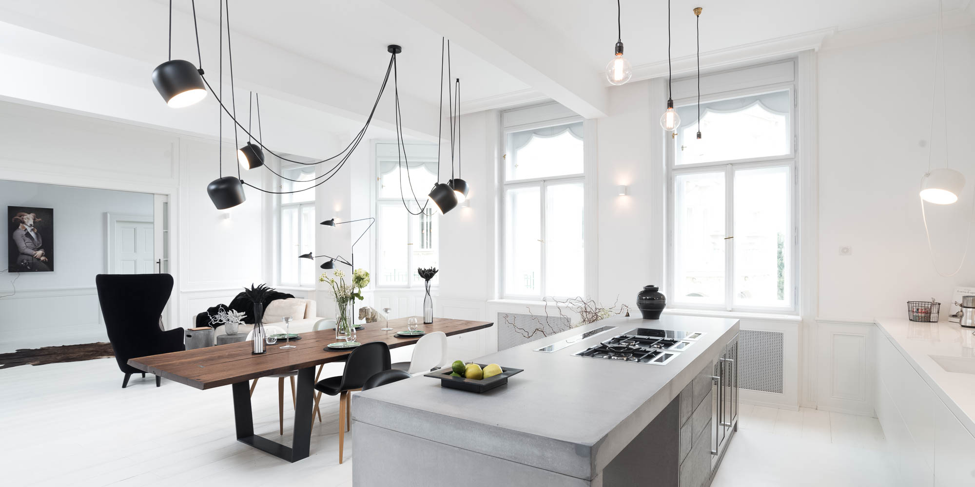 View into the living space with a concrete kitchen island, solid wood dining table and designer pendant light in an otherwise white interior | design by OOOOX