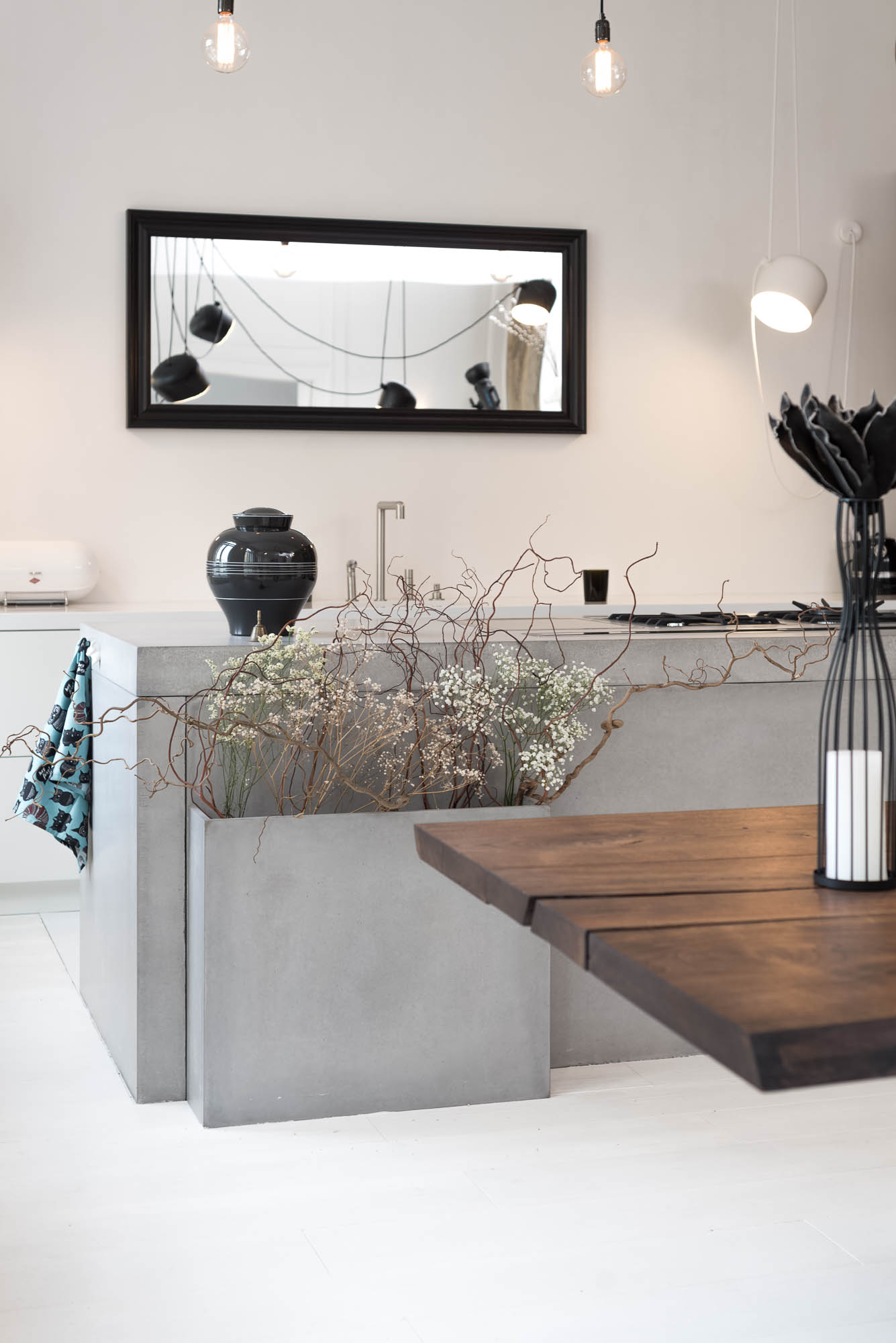 View of a kitchen island made from cast concrete slabs, integrated planter and mirror by the kitchen worktop visually extending the space | reconstruction design by OOOOX
