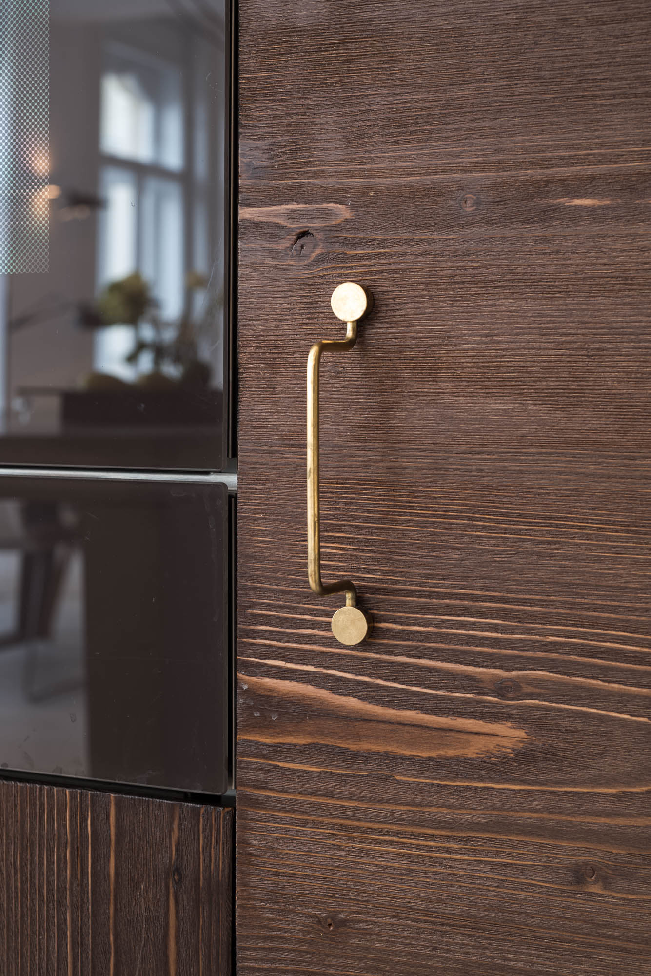 Detail of a delicate designer handle on a tall dark wood kitchen cabinet | design by OOOOX