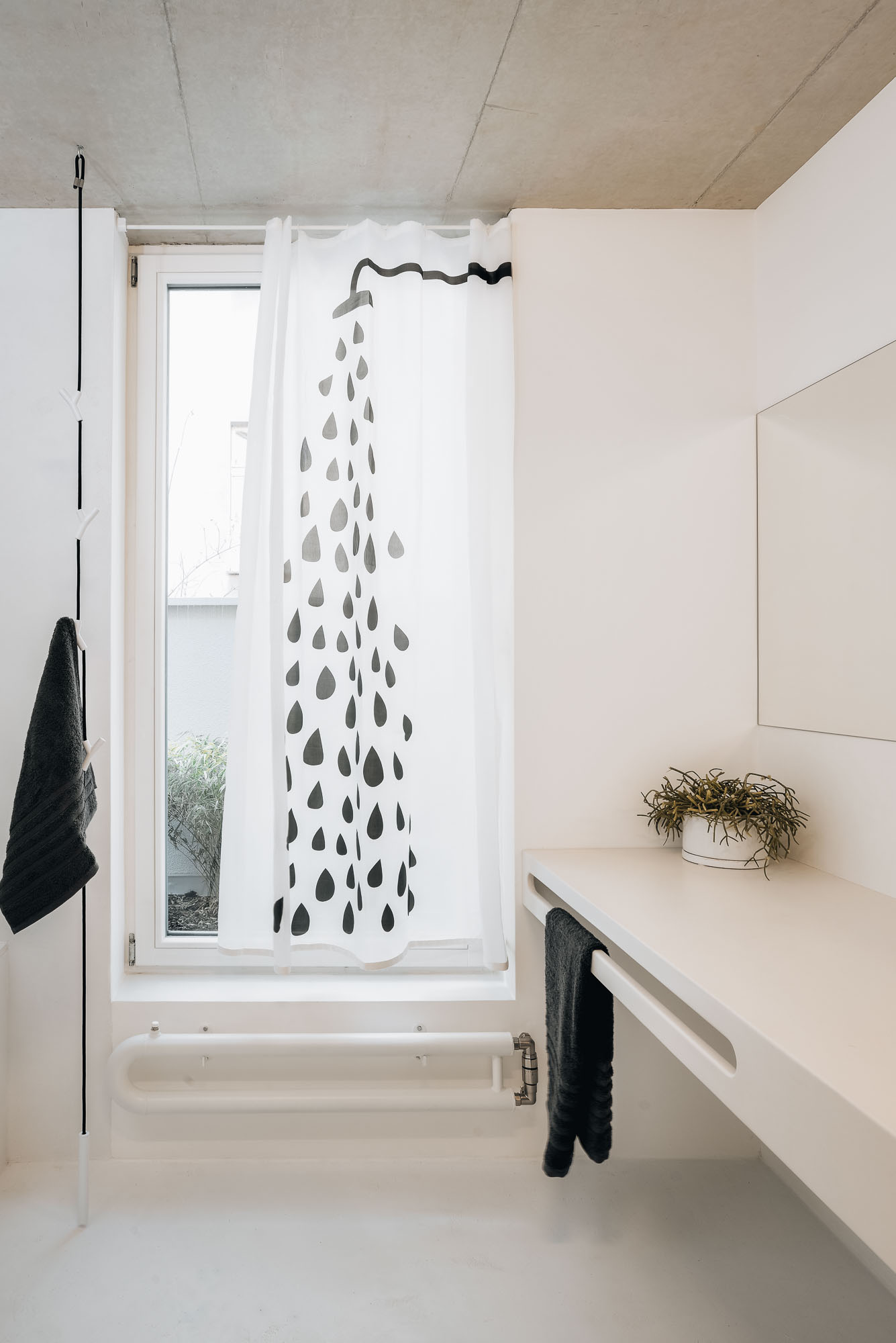 Detail of the bathroom vanity with a white cast marble countertop, stainless tap, and a decorative drop-pattern curtain at the window beside the mirror.