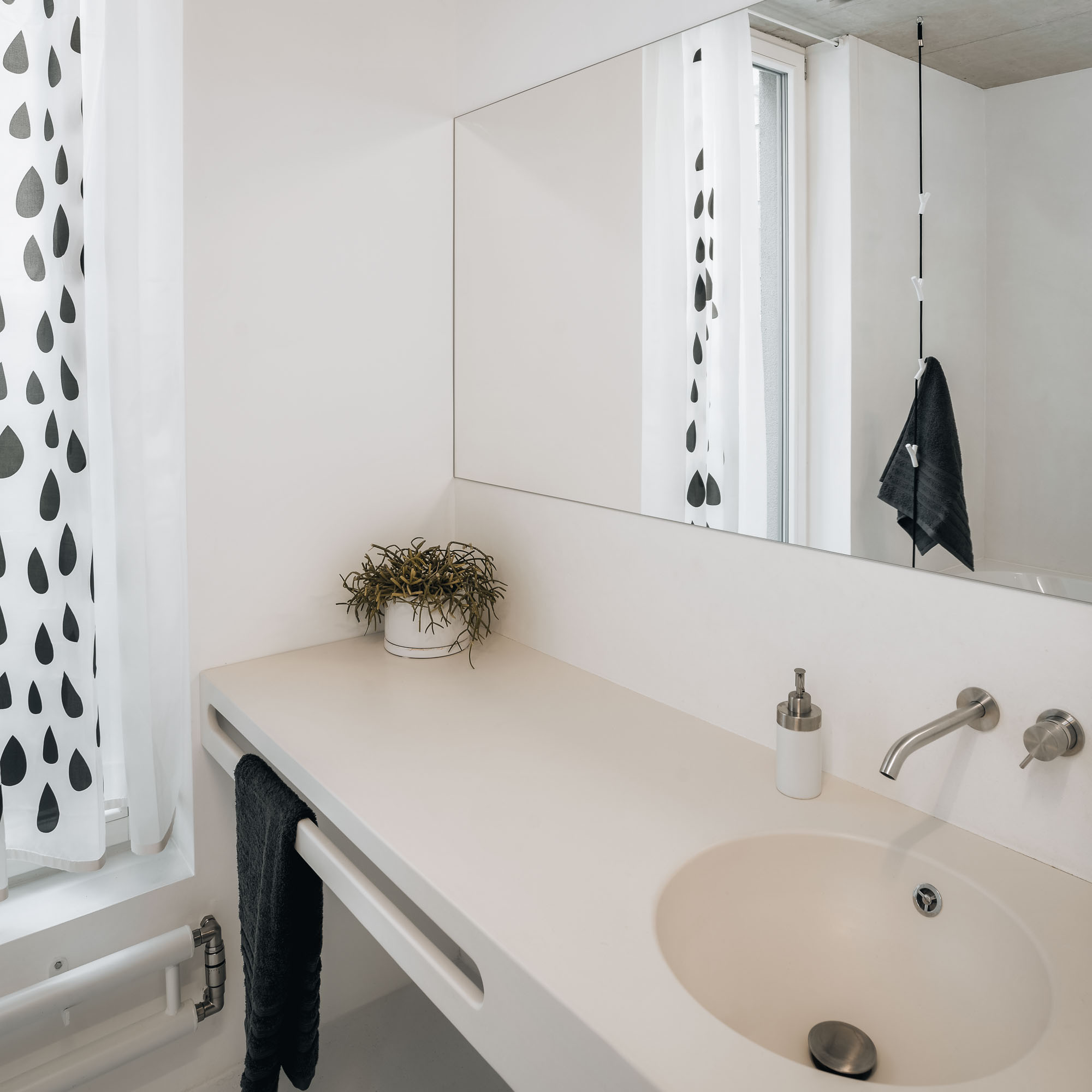 The upper-level bathroom with a white cast marble vanity counter and integrated basin, wall-mounted stainless steel tap, large mirror, decorative drop-pattern curtain, and exposed concrete ceiling
