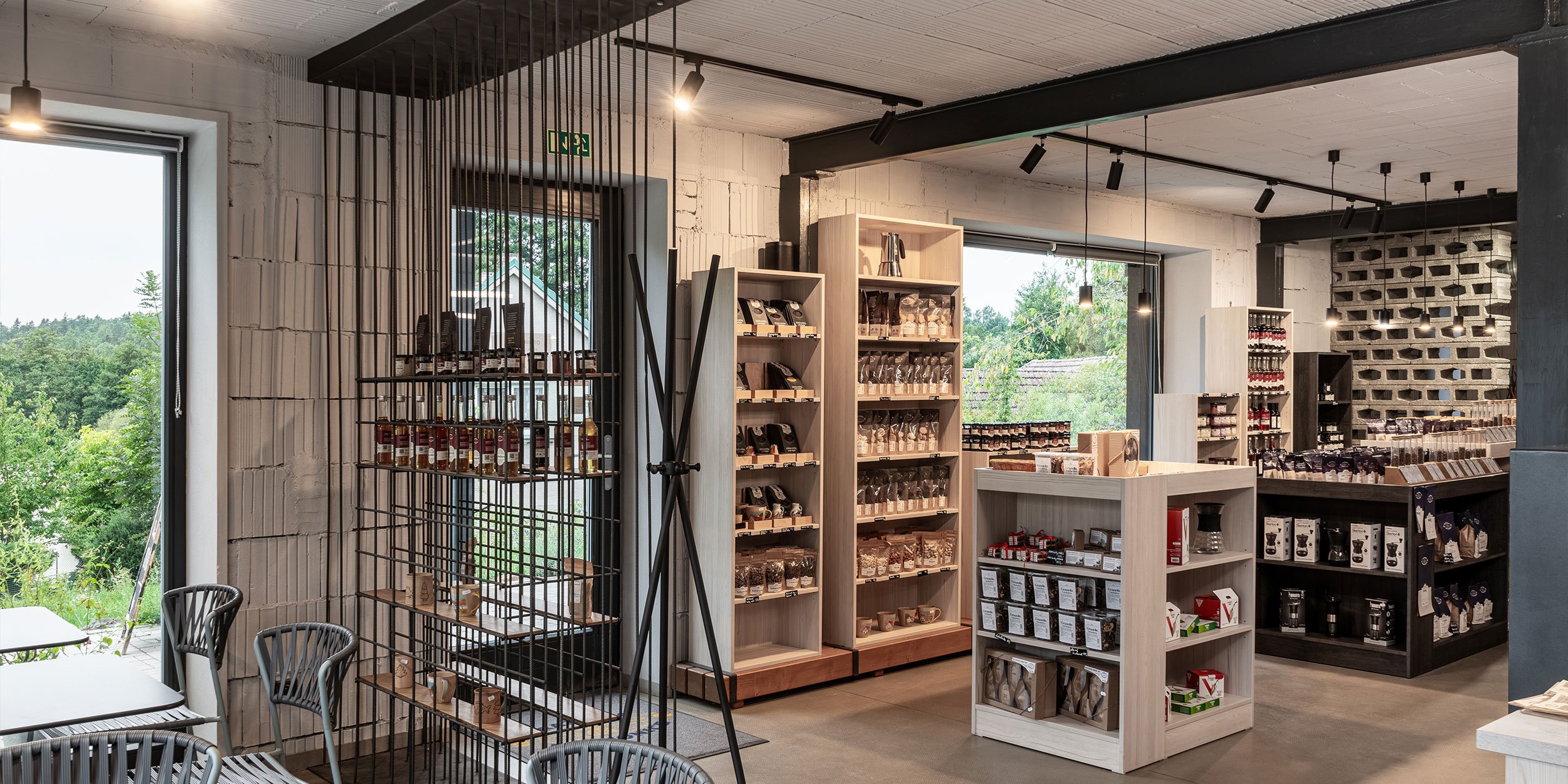Prodejna Pražírny Oltyně s světlými dřevěnými regály s produkty, roxorovým prostorovým dělítkem a velkými okny s výhledem do přírody