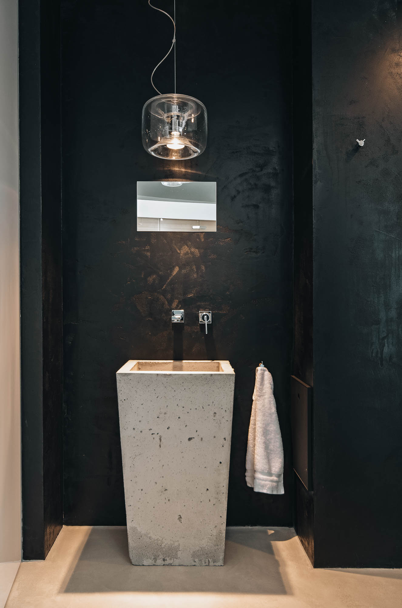 Betonové umyvadlo ve wellness koupelně vily s černou stěnou a skleněným svítidlem, OOOOX Praha